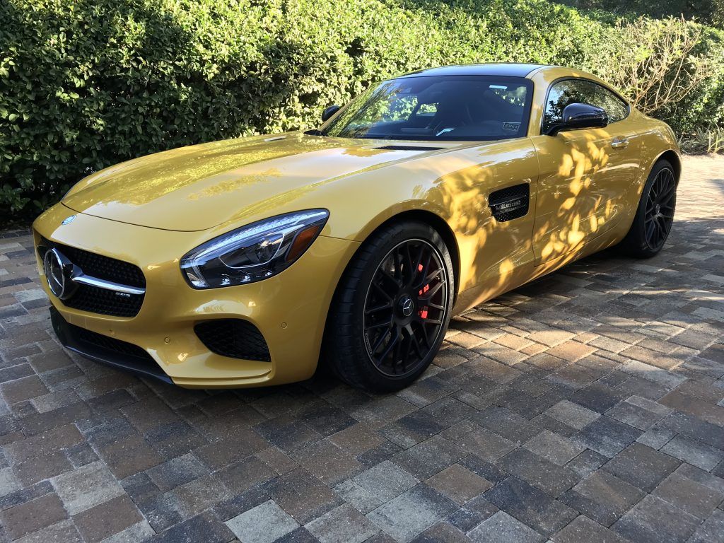 A yellow mercedes amg gt is parked on a brick driveway.