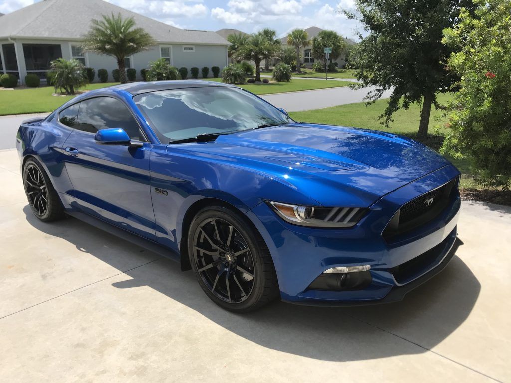A blue mustang is parked in a driveway in front of a house.