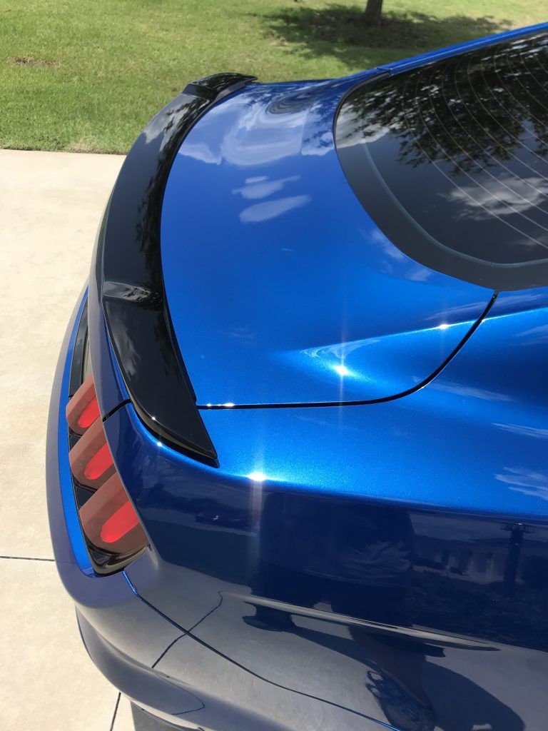 A blue car with a black spoiler is parked on the side of the road.