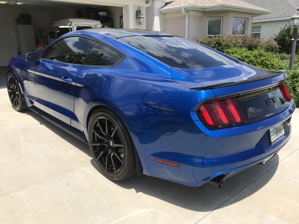 A blue mustang is parked in a driveway in front of a house.