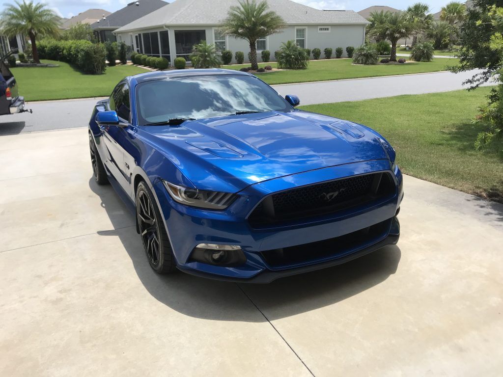 A blue mustang is parked in a driveway in front of a house