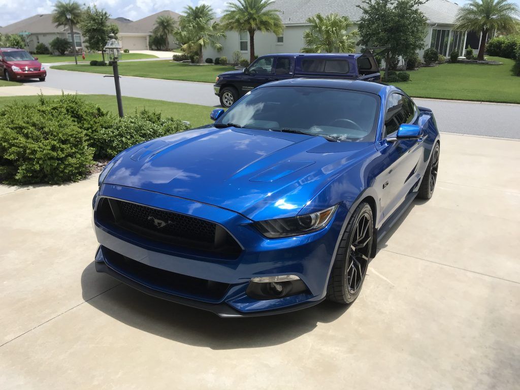 A blue mustang is parked in a driveway in front of a house.
