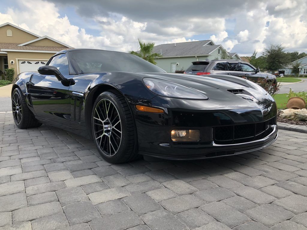 A black corvette is parked on a brick driveway in front of a house.