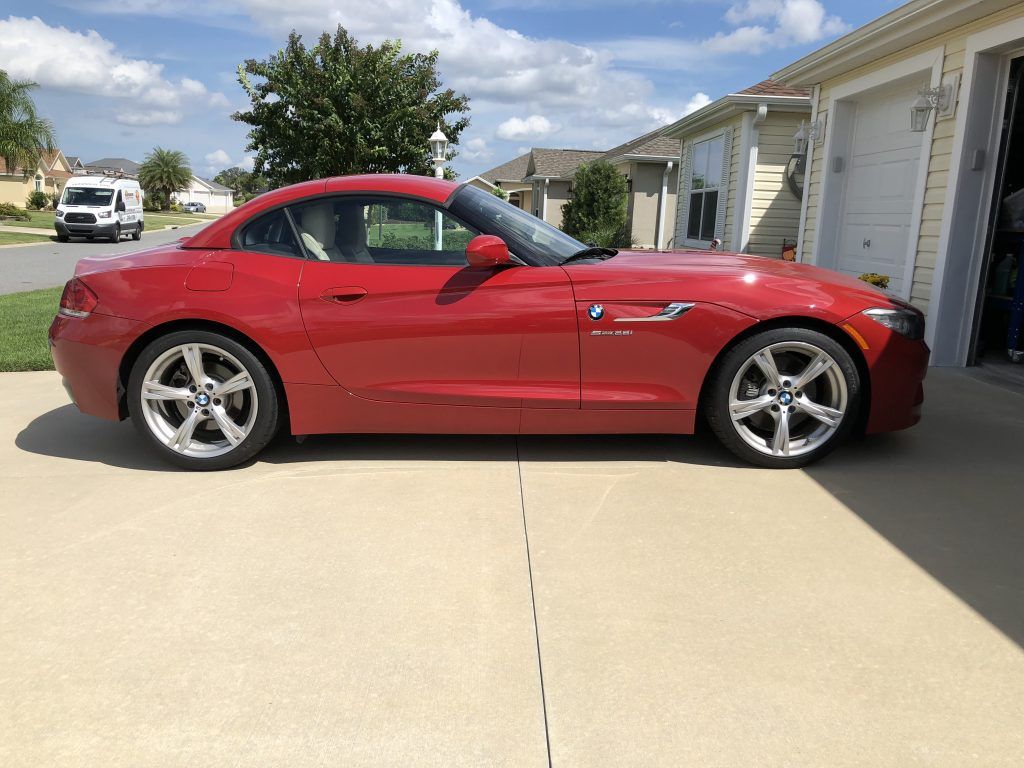 A red sports car is parked in a driveway next to a garage.