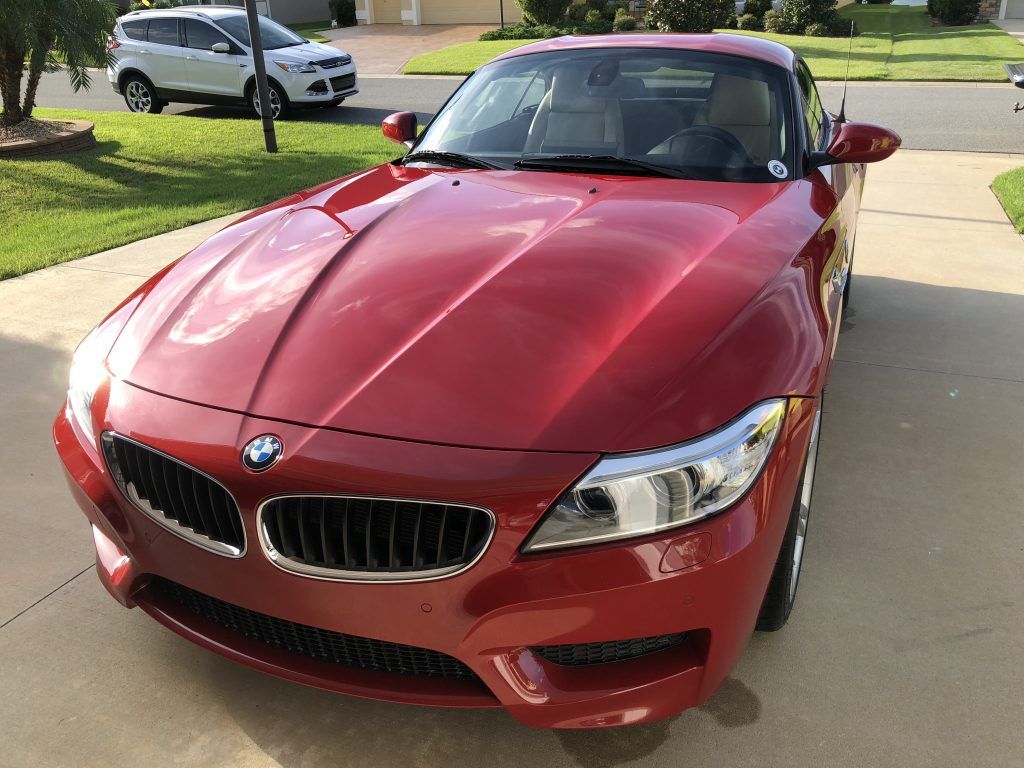A red bmw z4 is parked in a driveway next to a white suv.