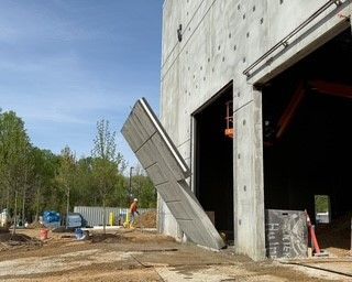 A man is standing in front of a large concrete building under construction.