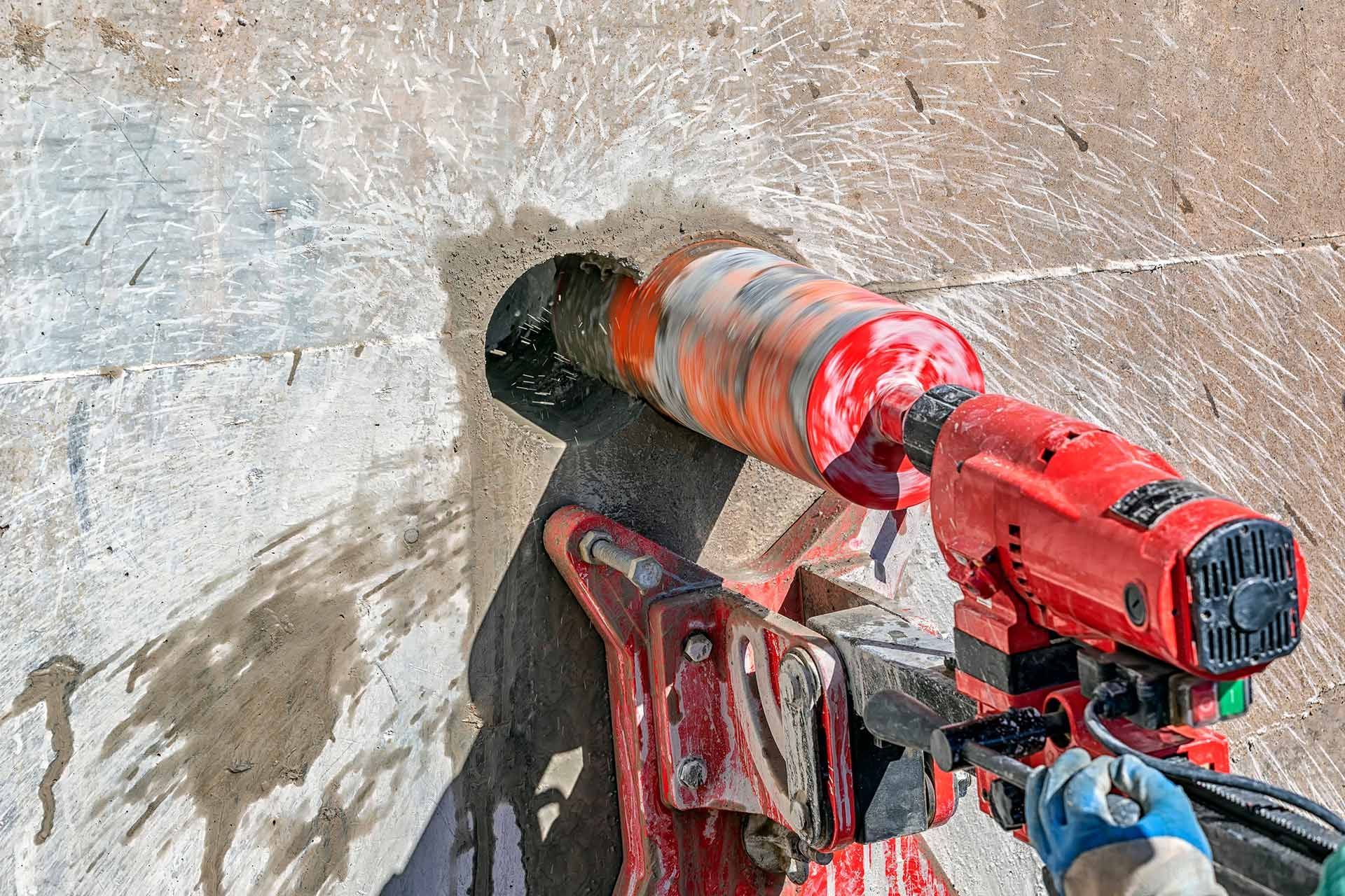 Worker drilling a precise hole into a concrete wall using industrial drilling equipment.