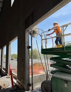 Construction worker on a lift using a concrete saw to cut a doorway into a building wall.