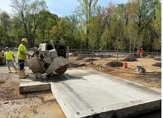 Construction workers using a saw to cut concrete on a construction site. Trees are in the background.