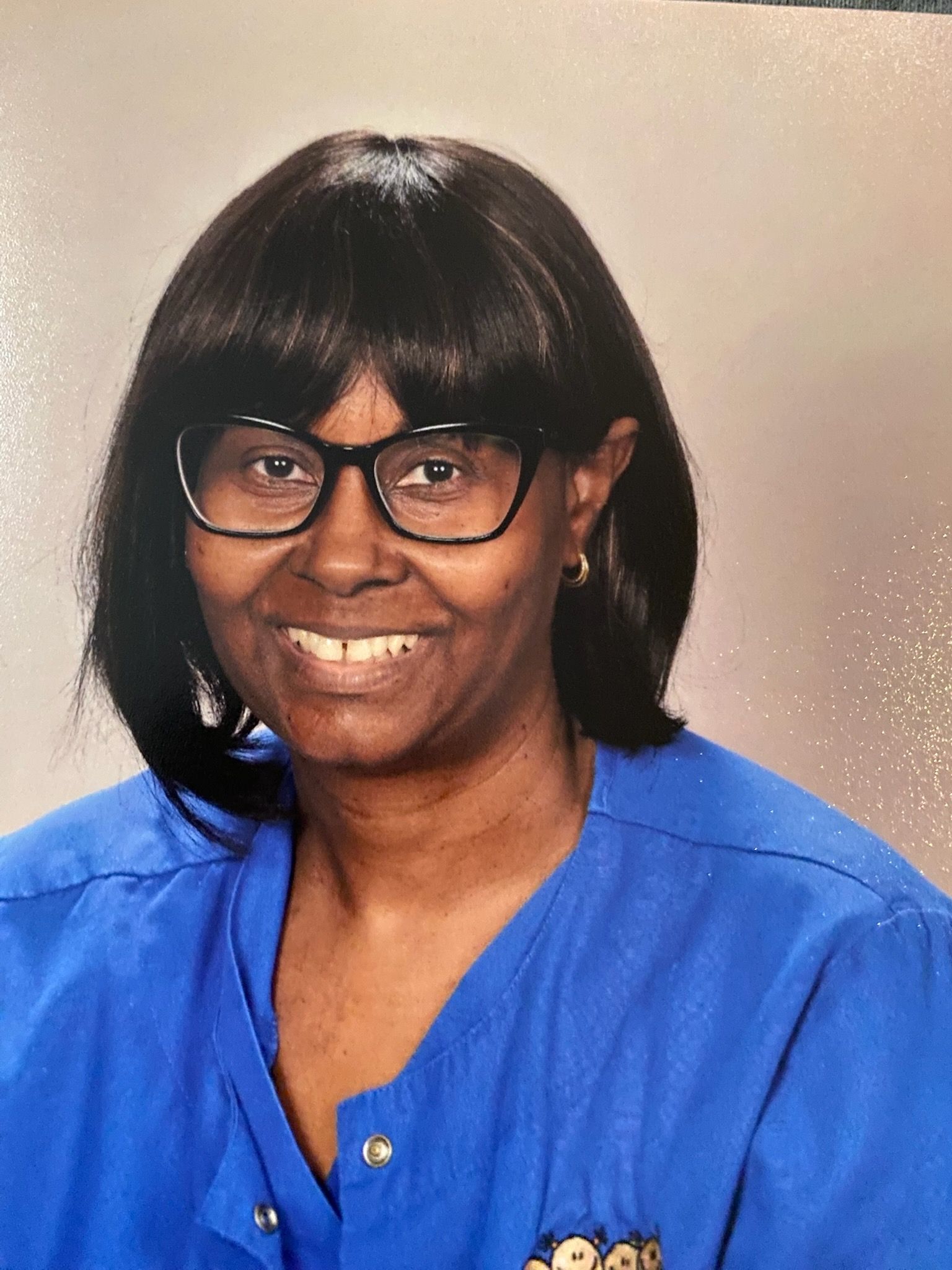 Woman wearing glasses, smiling, in a blue shirt; head and shoulders shot.