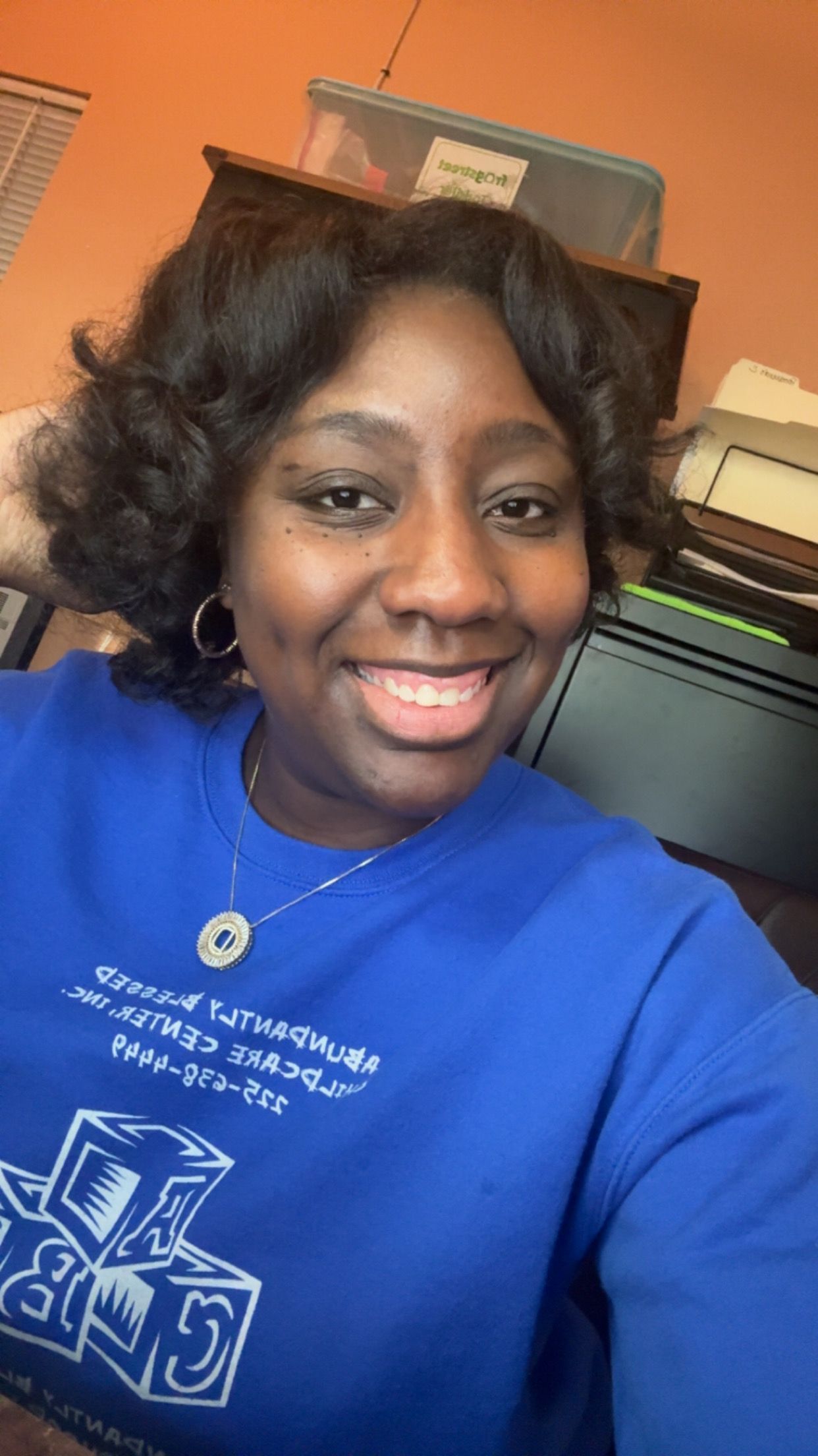 Woman smiling in a blue shirt with text, indoors.