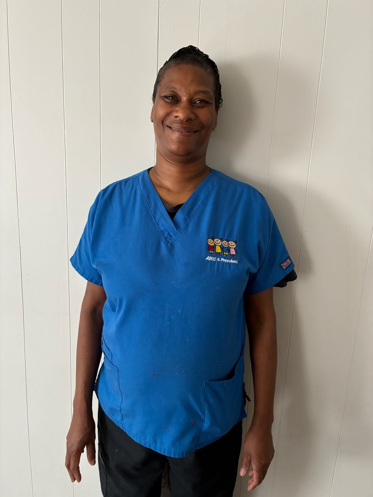 Person in blue scrubs smiles in front of a white wall.