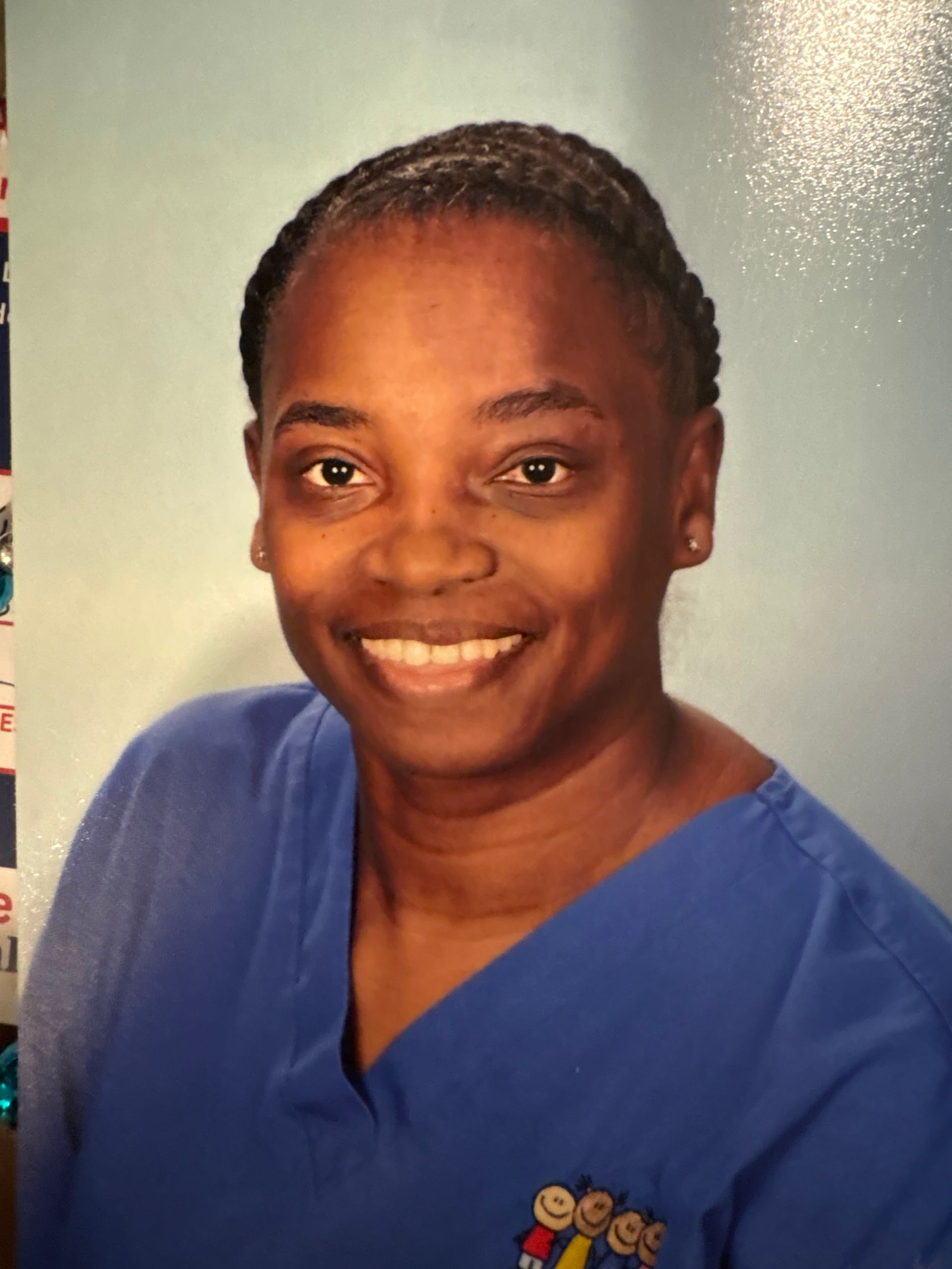 Woman in blue scrubs smiles, looking at the camera.