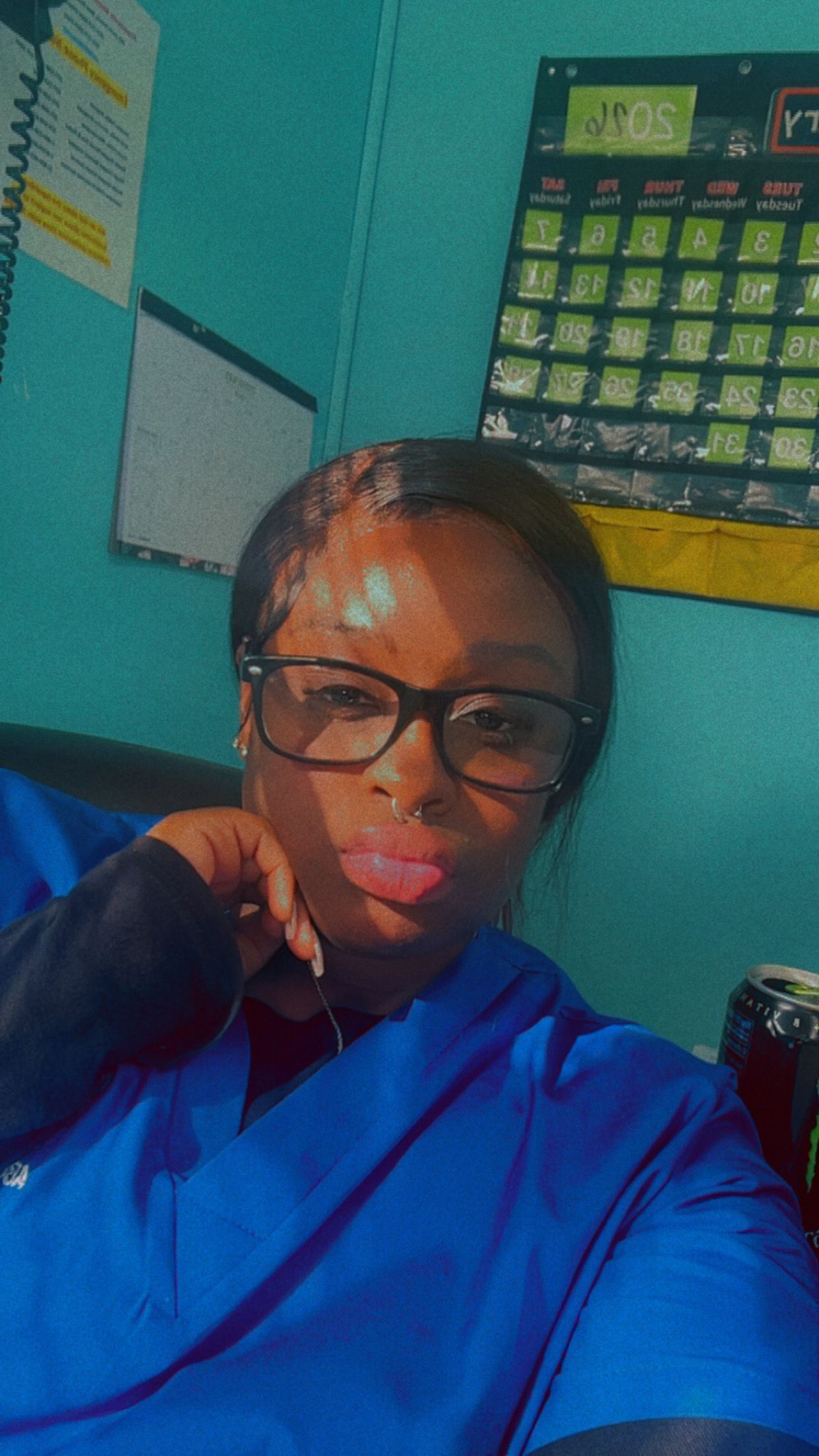 Woman wearing glasses and blue scrubs in front of a calendar.