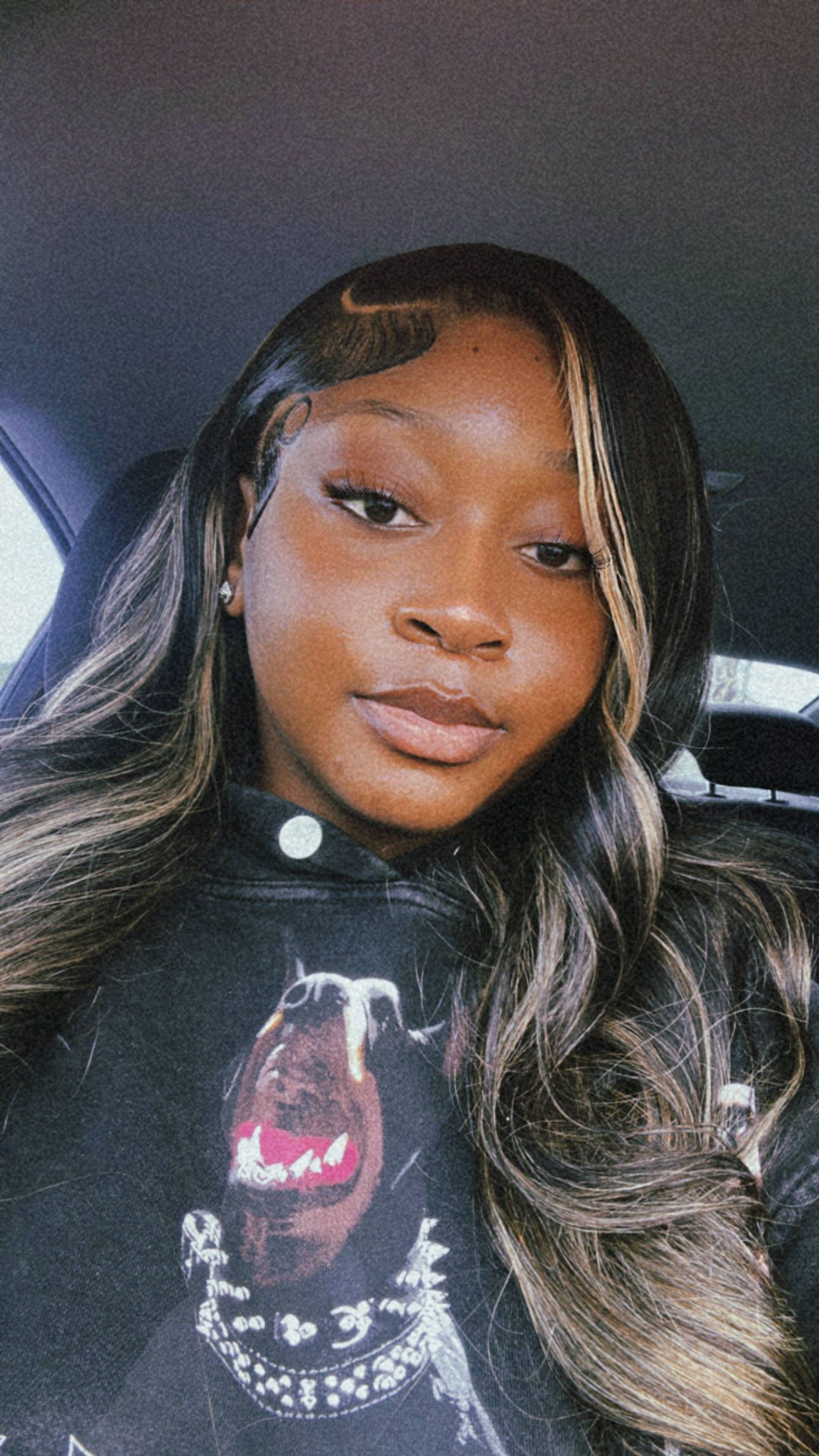 Woman in a black hoodie with a dog graphic, long wavy hair with blonde highlights, looking at the camera.