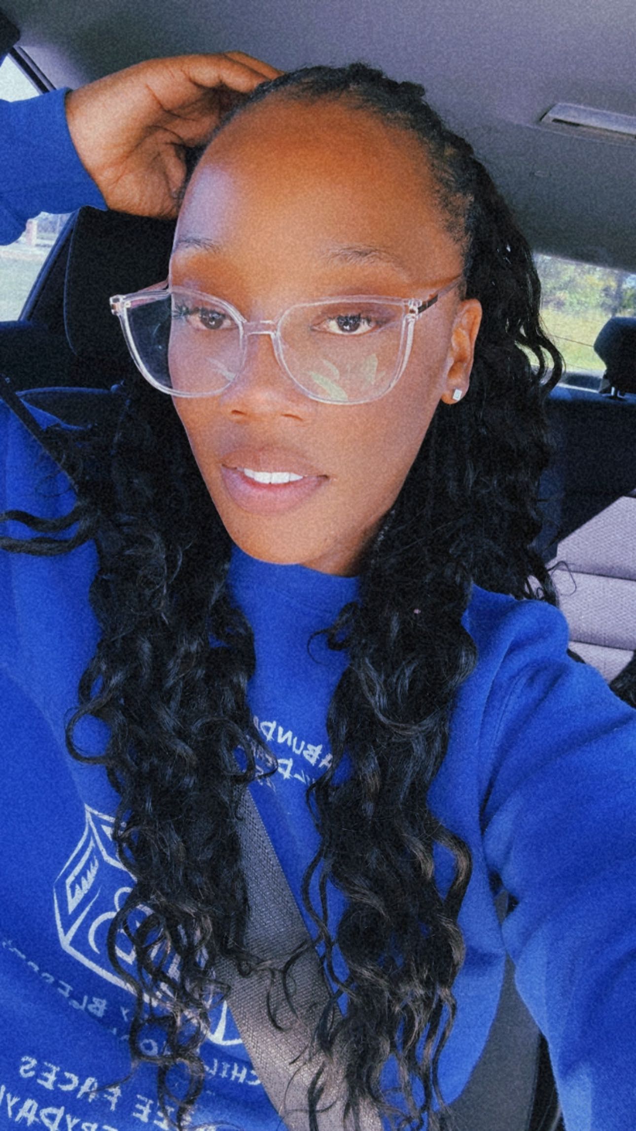 Person with wavy black hair wearing glasses and blue sweatshirt.