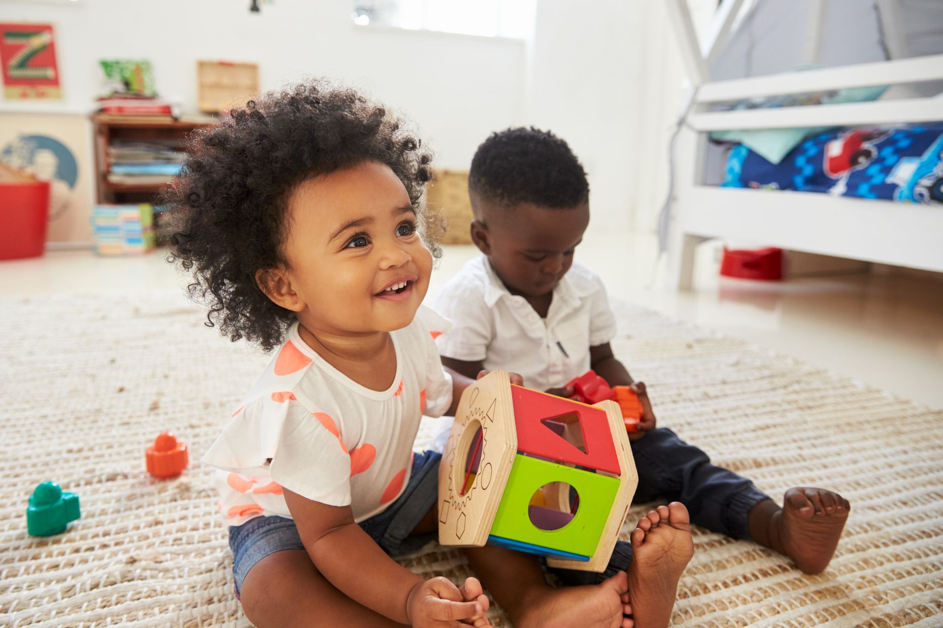 Two babies are sitting on the floor playing with toys.