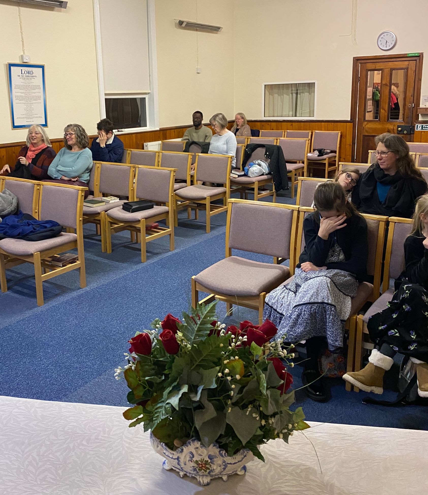 A group of people are sitting in chairs in a room with a vase of flowers in the foreground