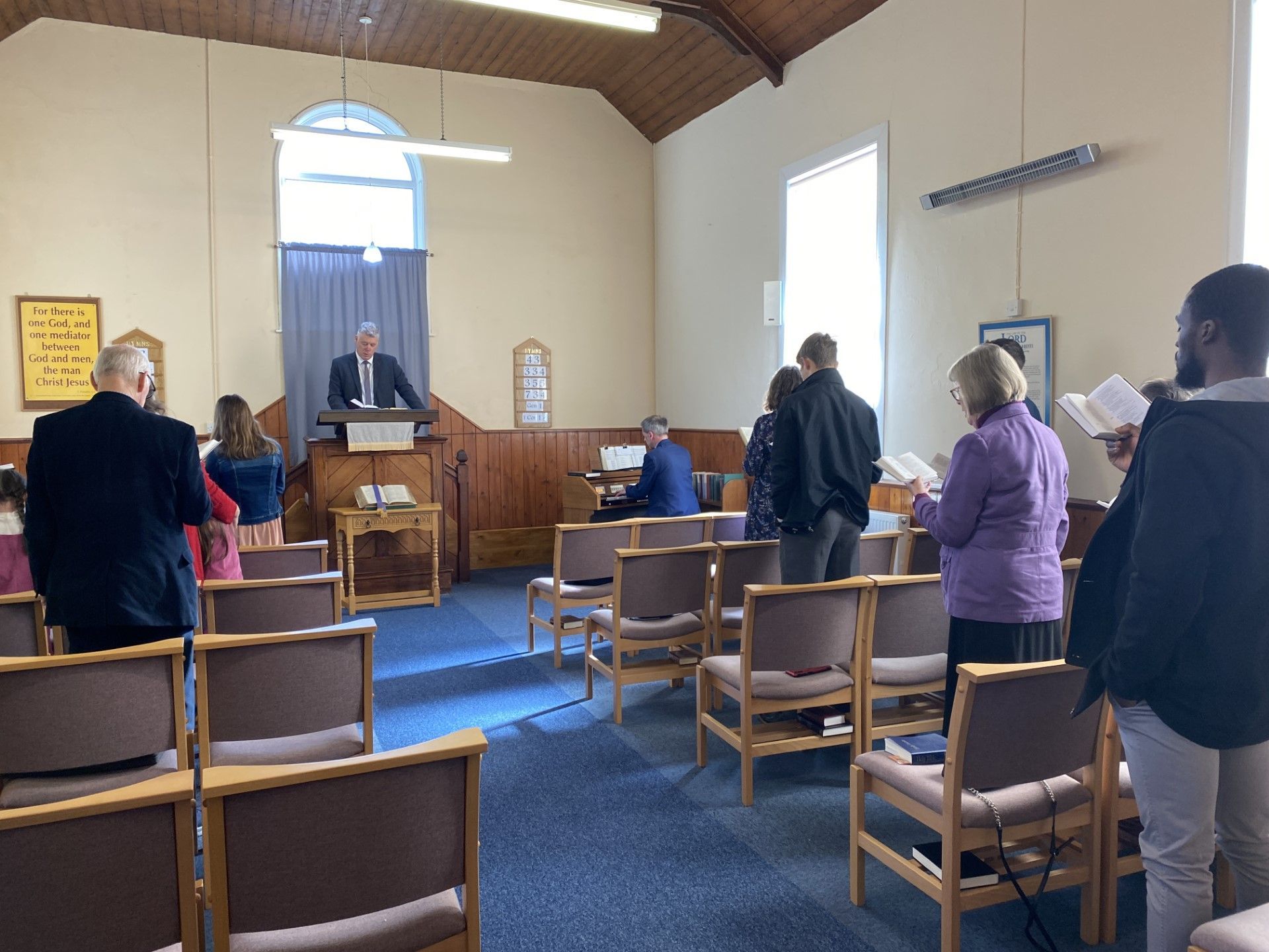 A group of people are standing in a church while a man stands at a podium.