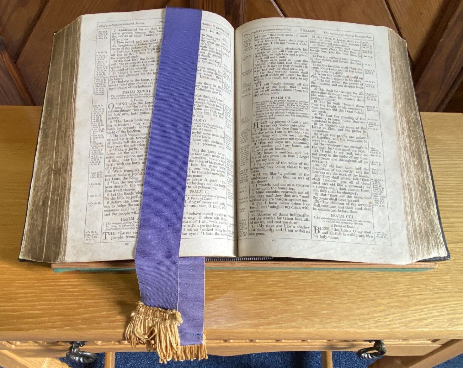 An open bible with a purple bookmark on a wooden table.