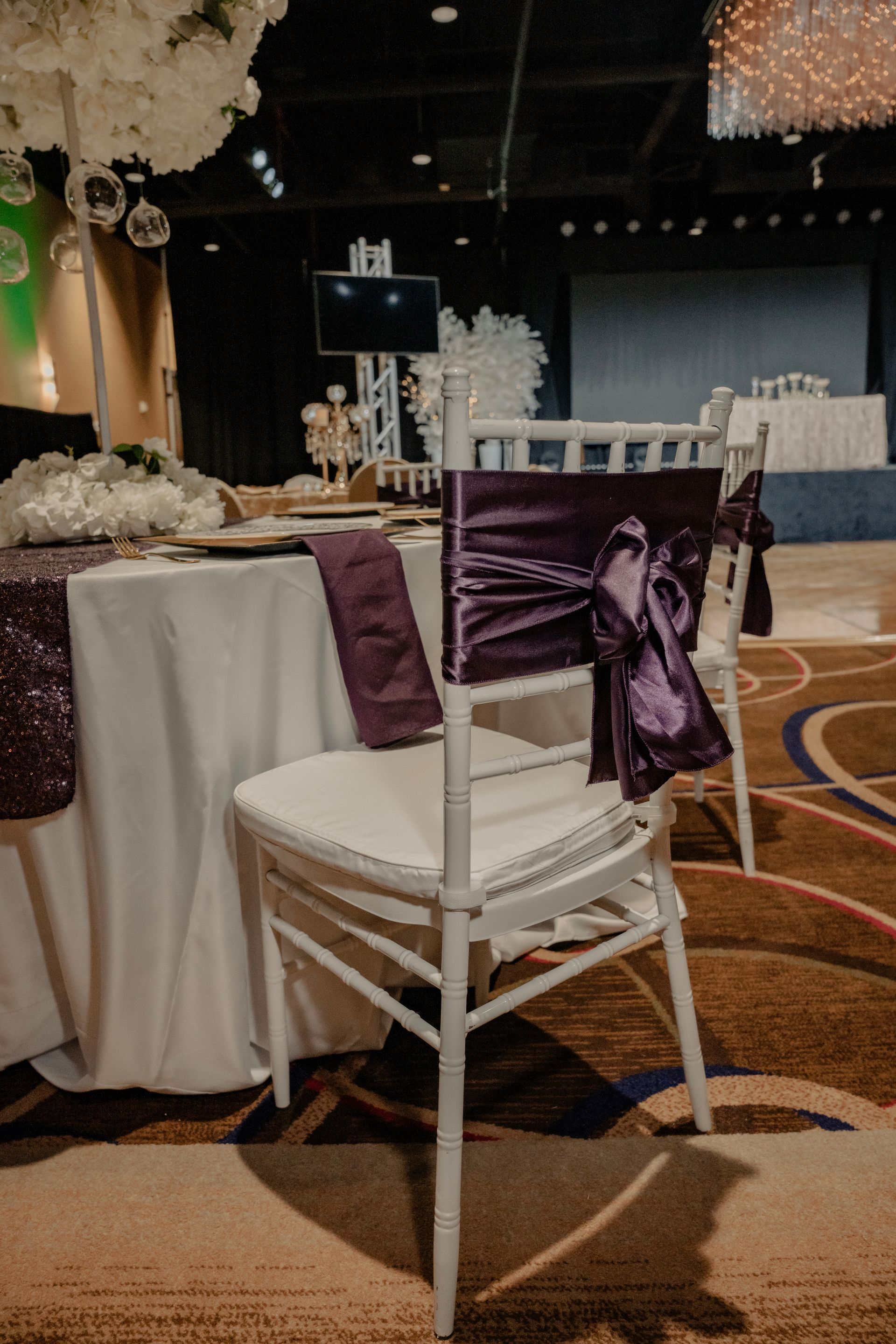 A white chair with a purple bow on the back is sitting in front of a table.