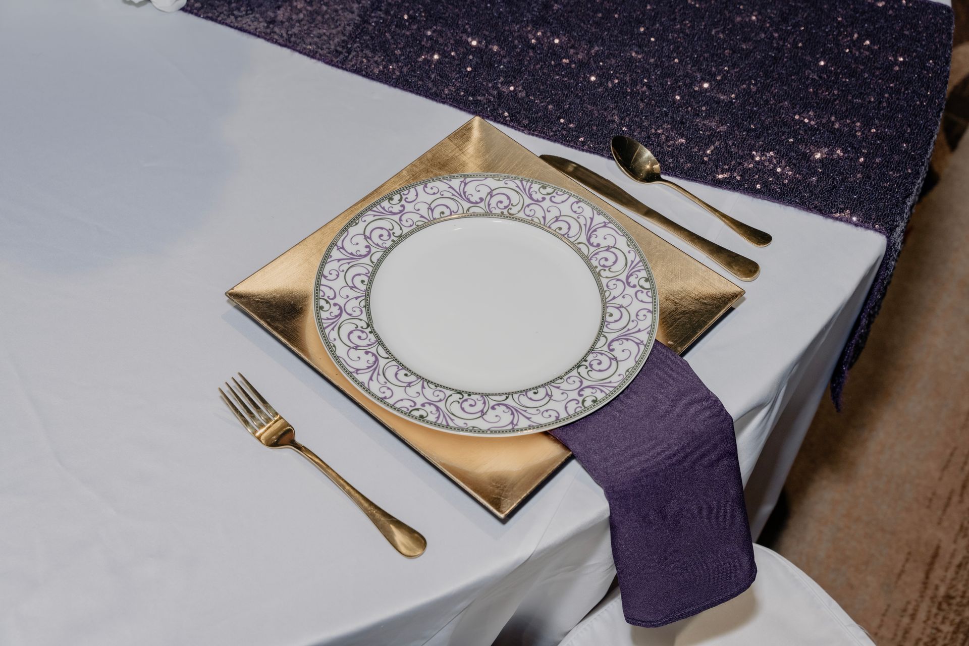 A white plate with a purple napkin and gold silverware on a table.