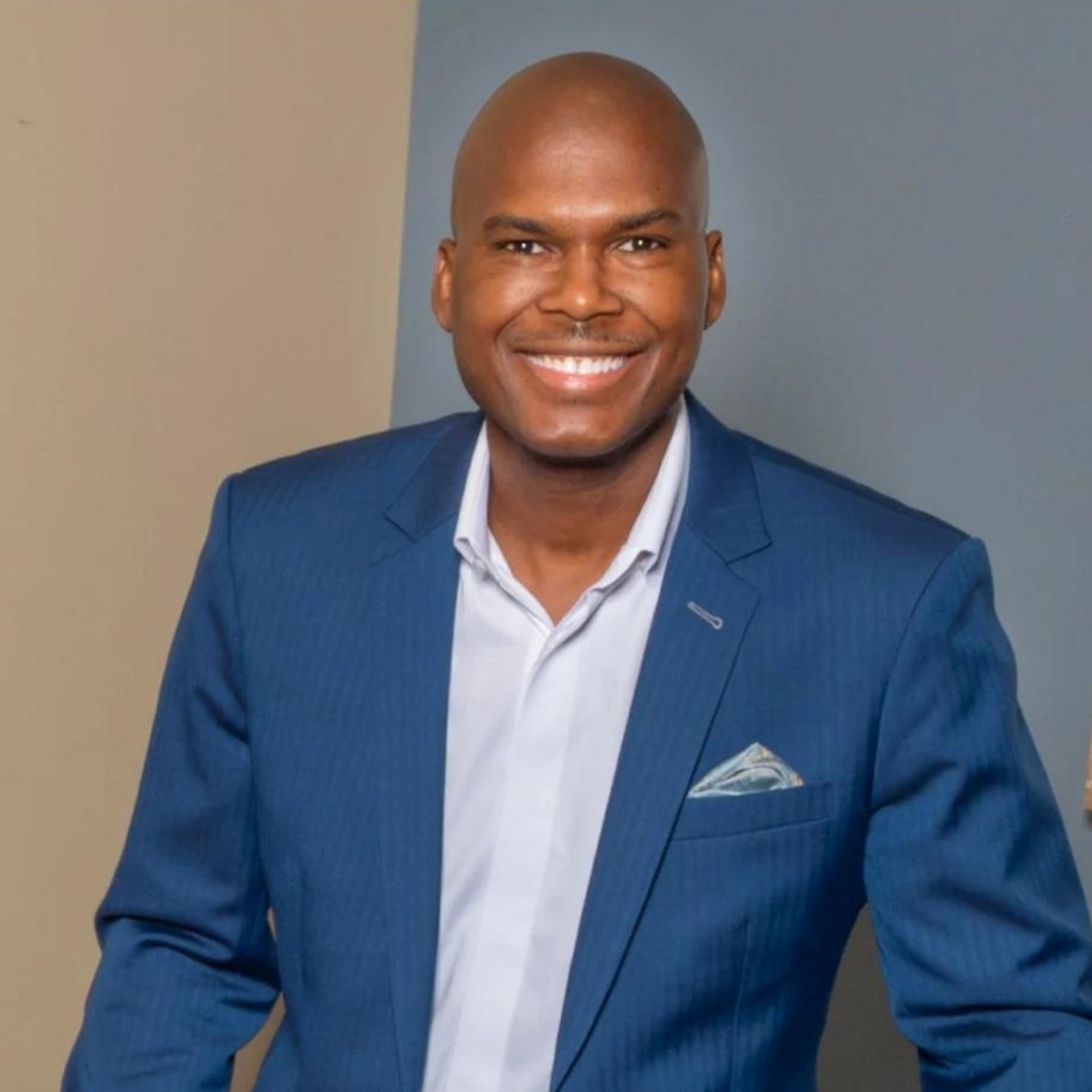 A man in a blue suit and white shirt smiles for the camera