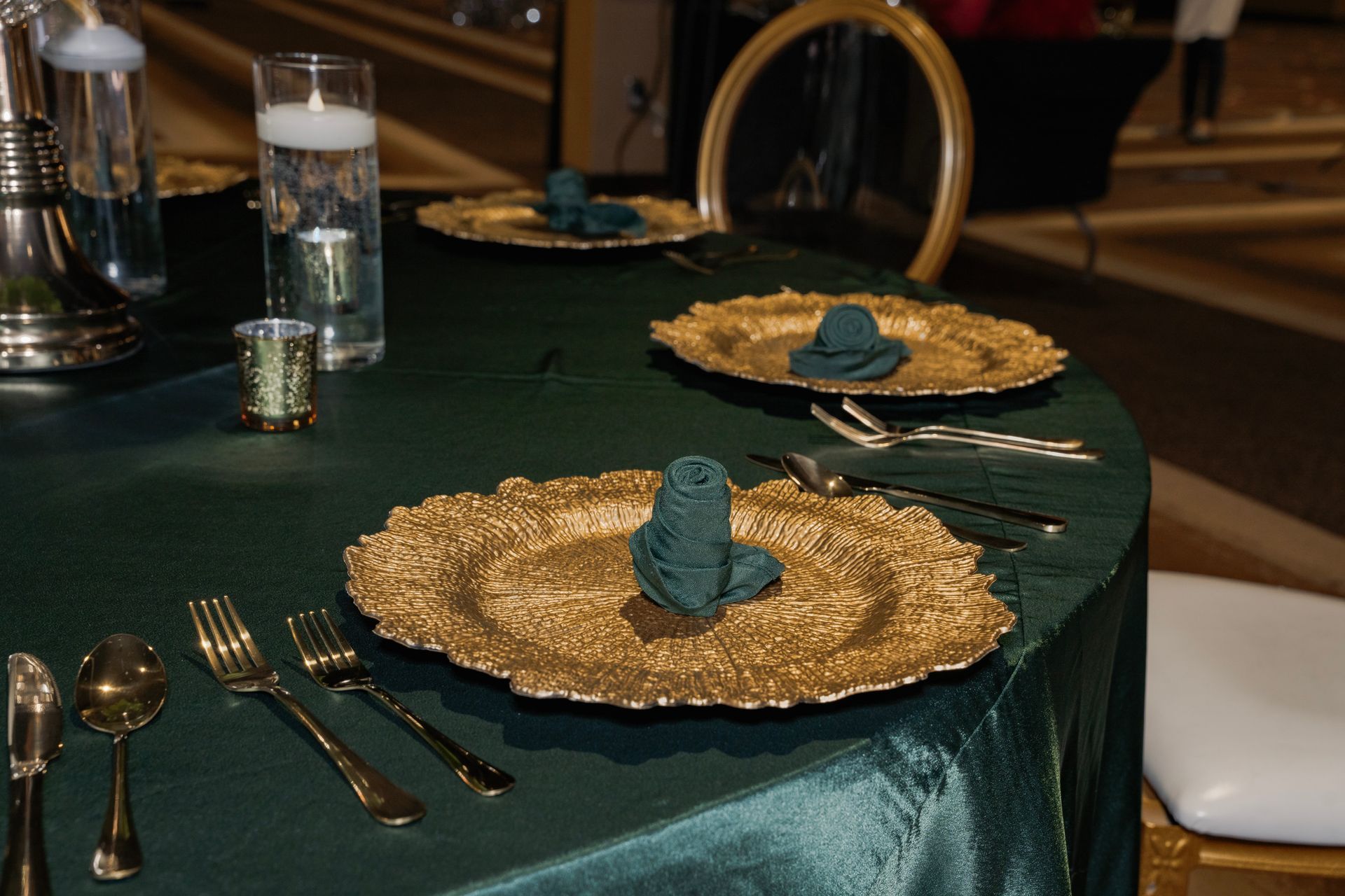 A green table cloth with gold plates and silverware on it