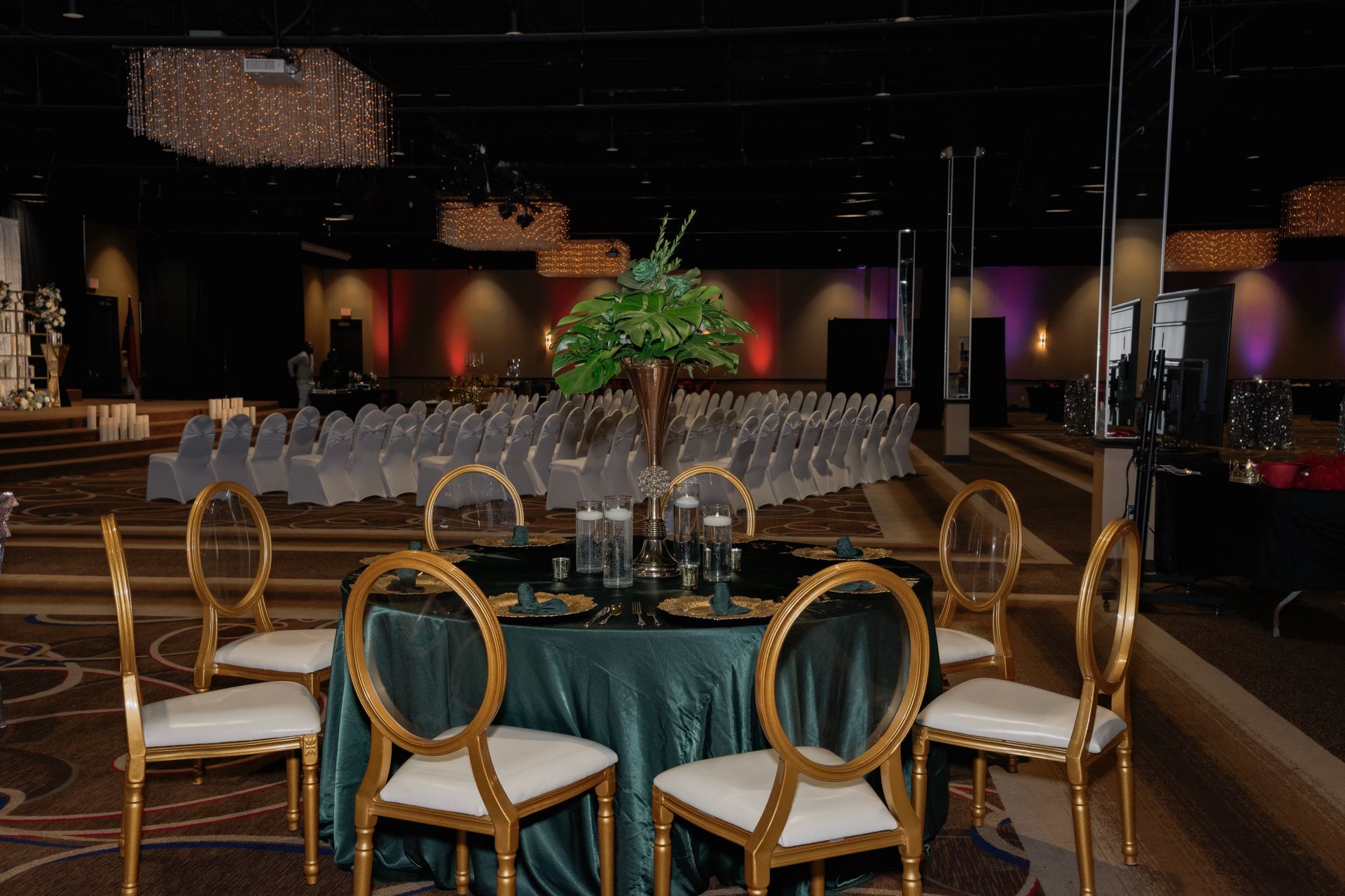 A table with a green tablecloth and gold chairs in a large room.