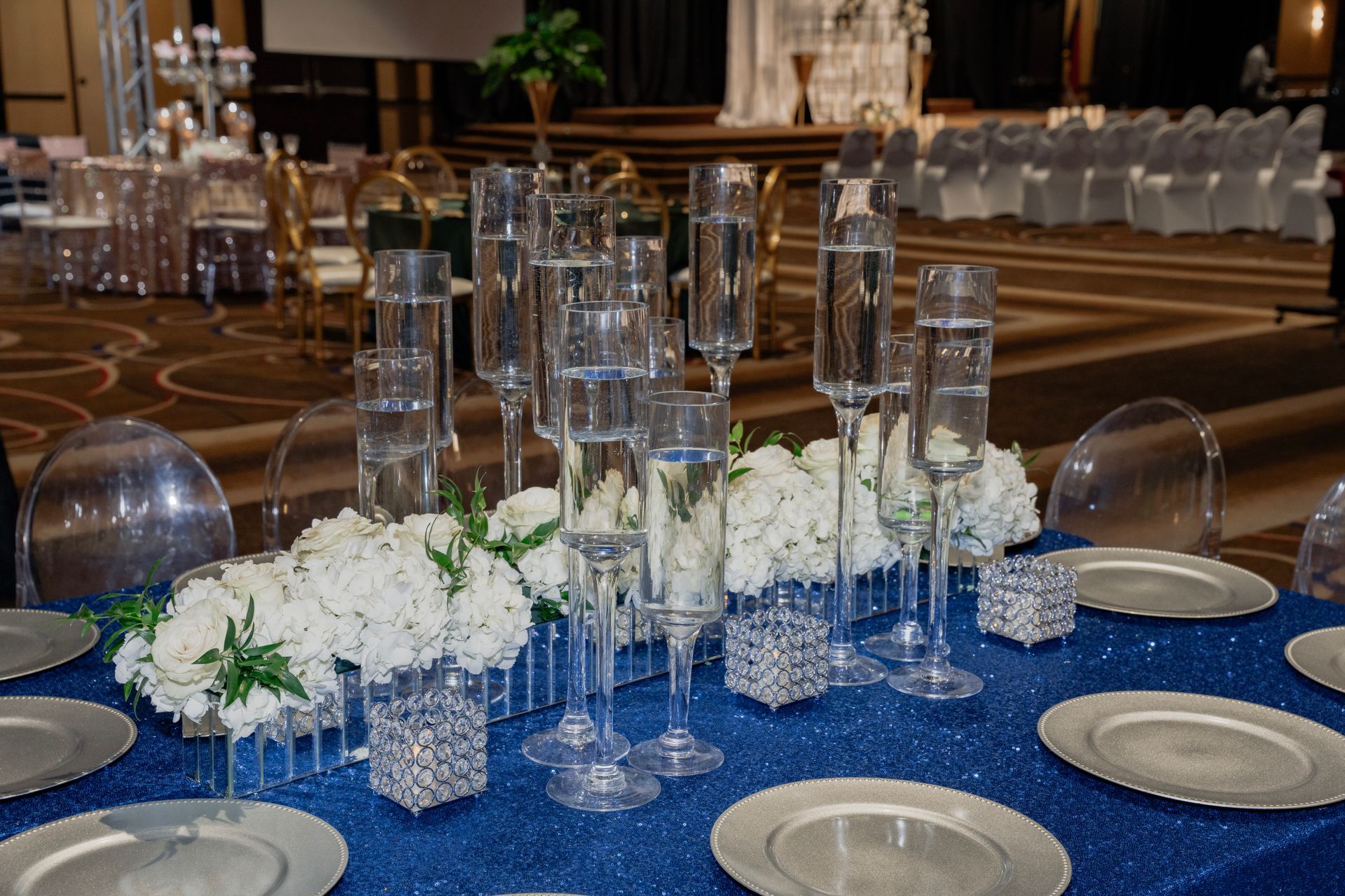 A table set for a wedding reception with plates , glasses , and flowers on it.