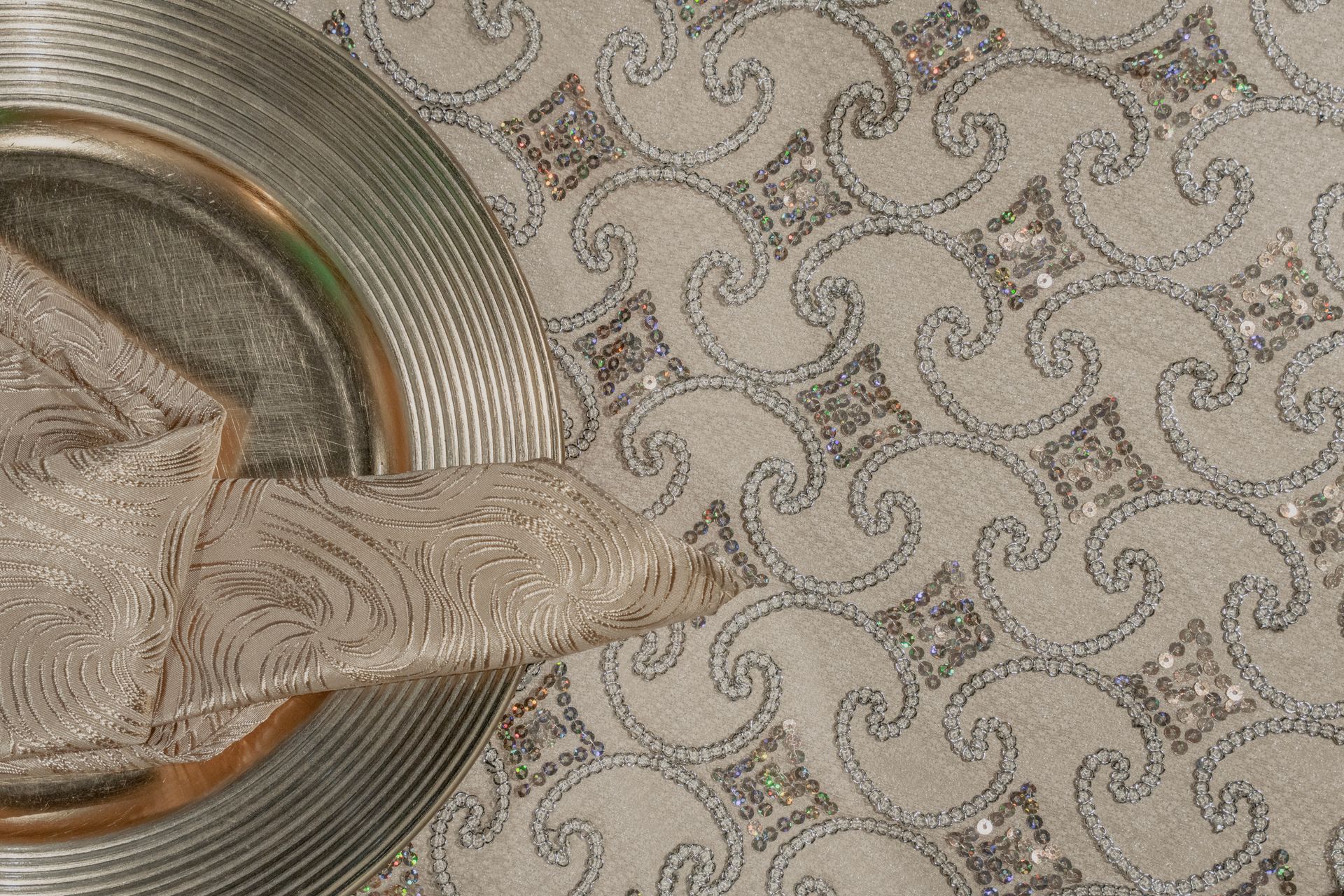 A silver plate with a napkin on it is on a table with a silver table cloth.