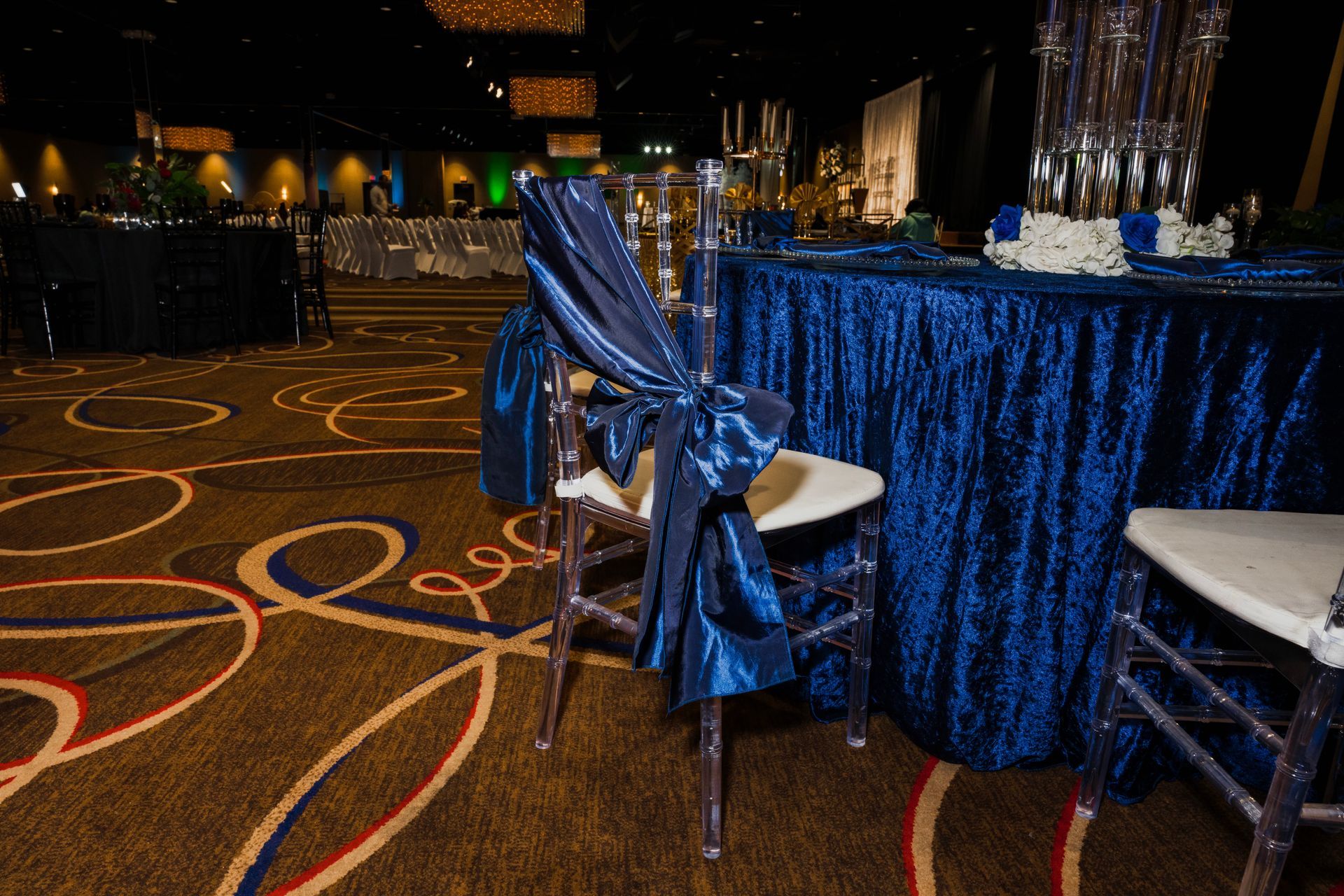 A chair with a blue bow is sitting in front of a table with a blue table cloth.