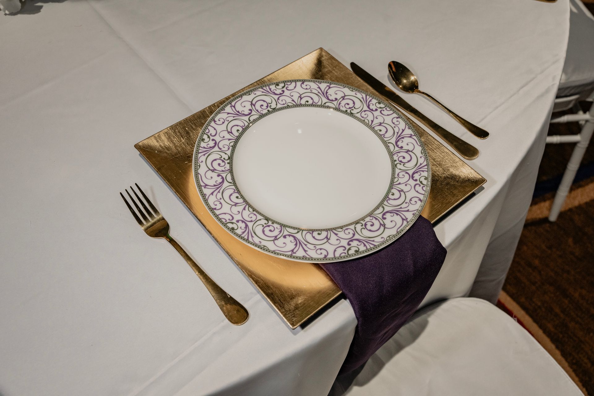 A white plate with a purple napkin is on a table with silverware.