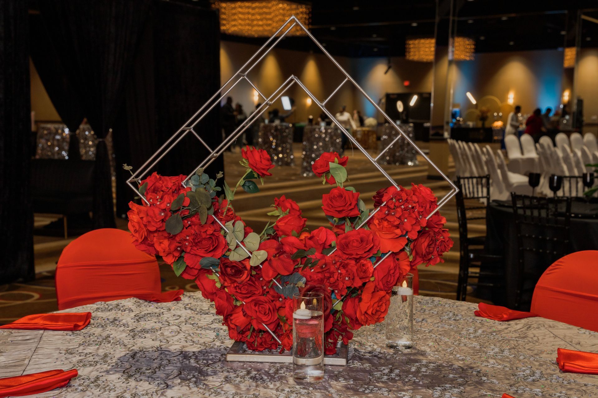 A table with a vase of red flowers and candles on it.