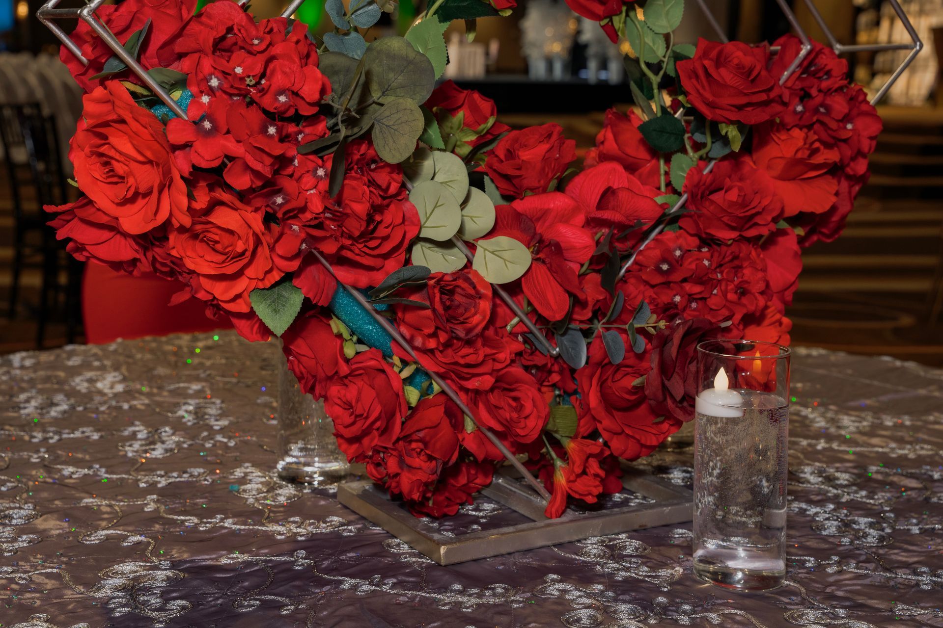 A heart shaped vase filled with red roses and a candle on a table.
