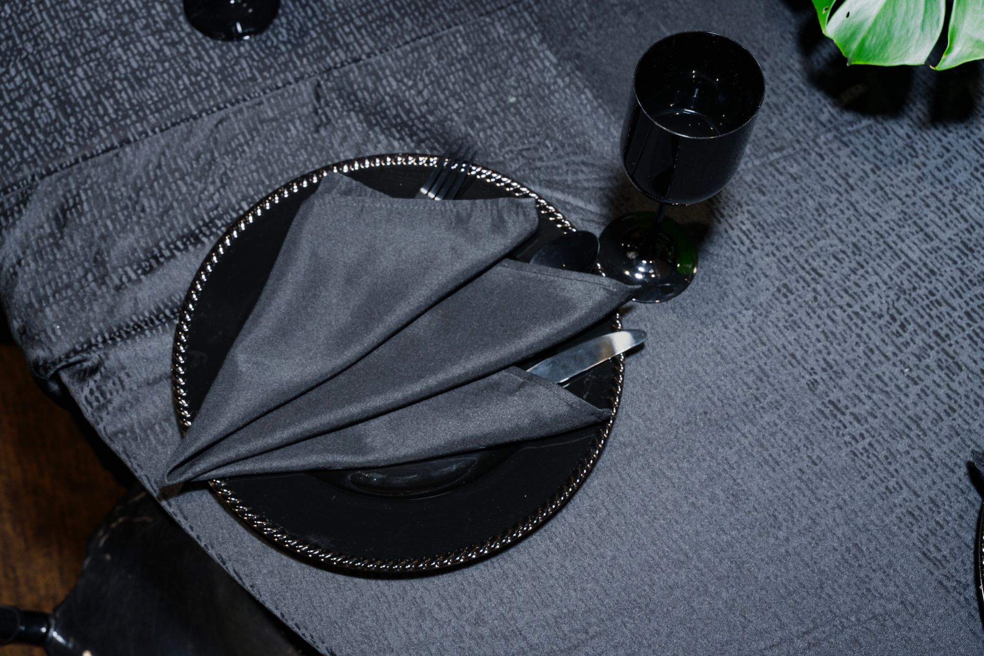 A black plate with a black napkin and a black glass on a table.