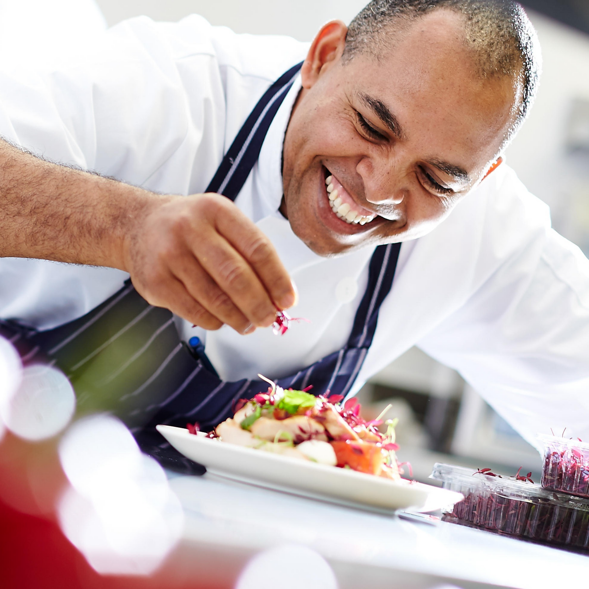 A man in an apron is smiling while decorating a plate of food