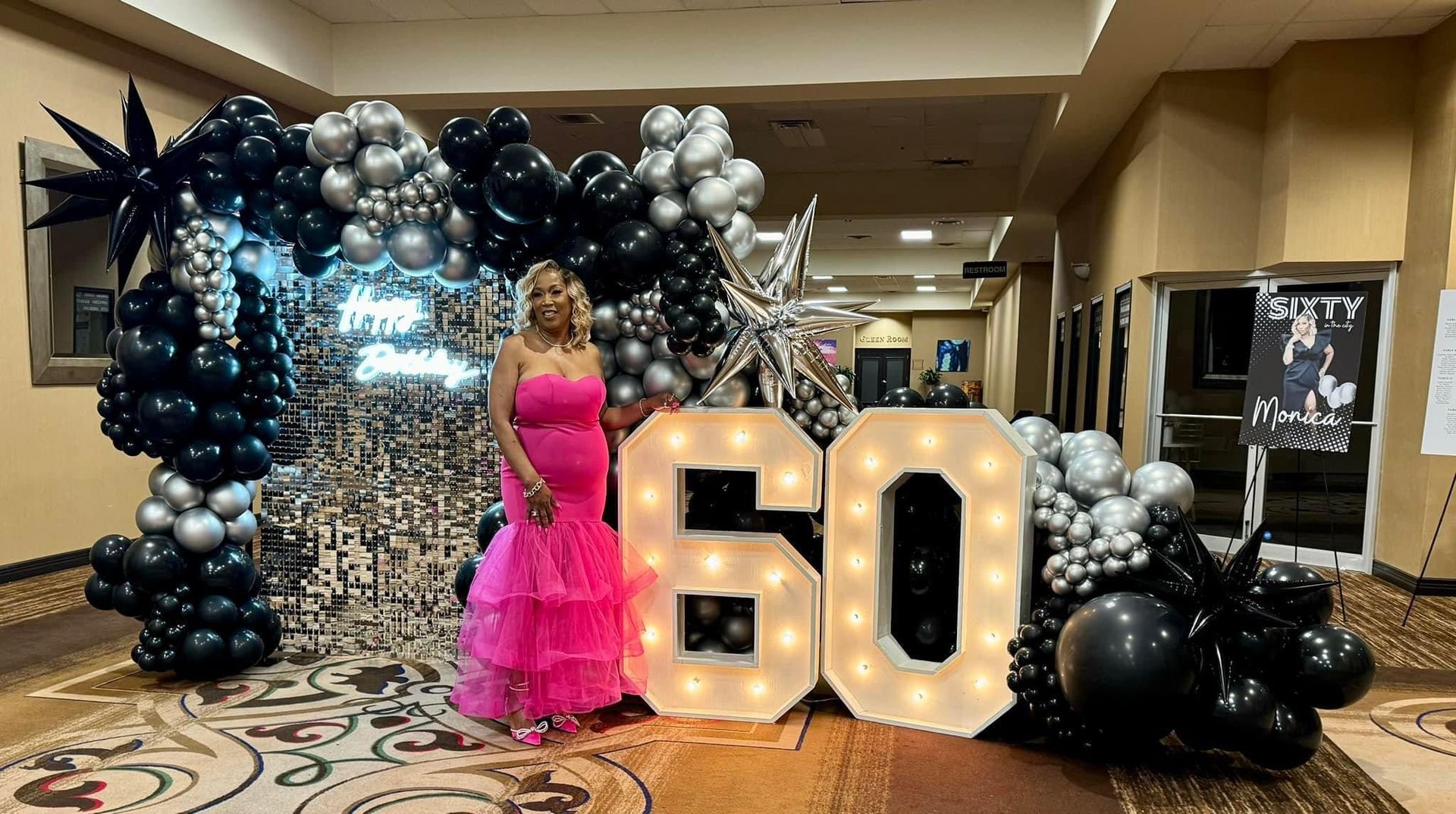 A woman in a pink dress is standing in front of a wall of balloons.