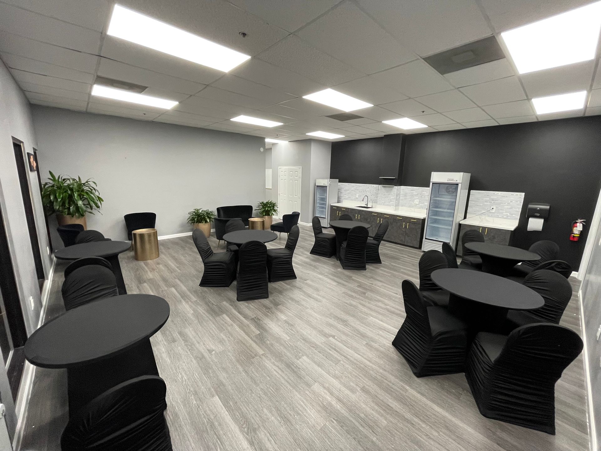 The Collective Lounge set up with black tables, chairs, and dark grey walls, with a small kitchen area.