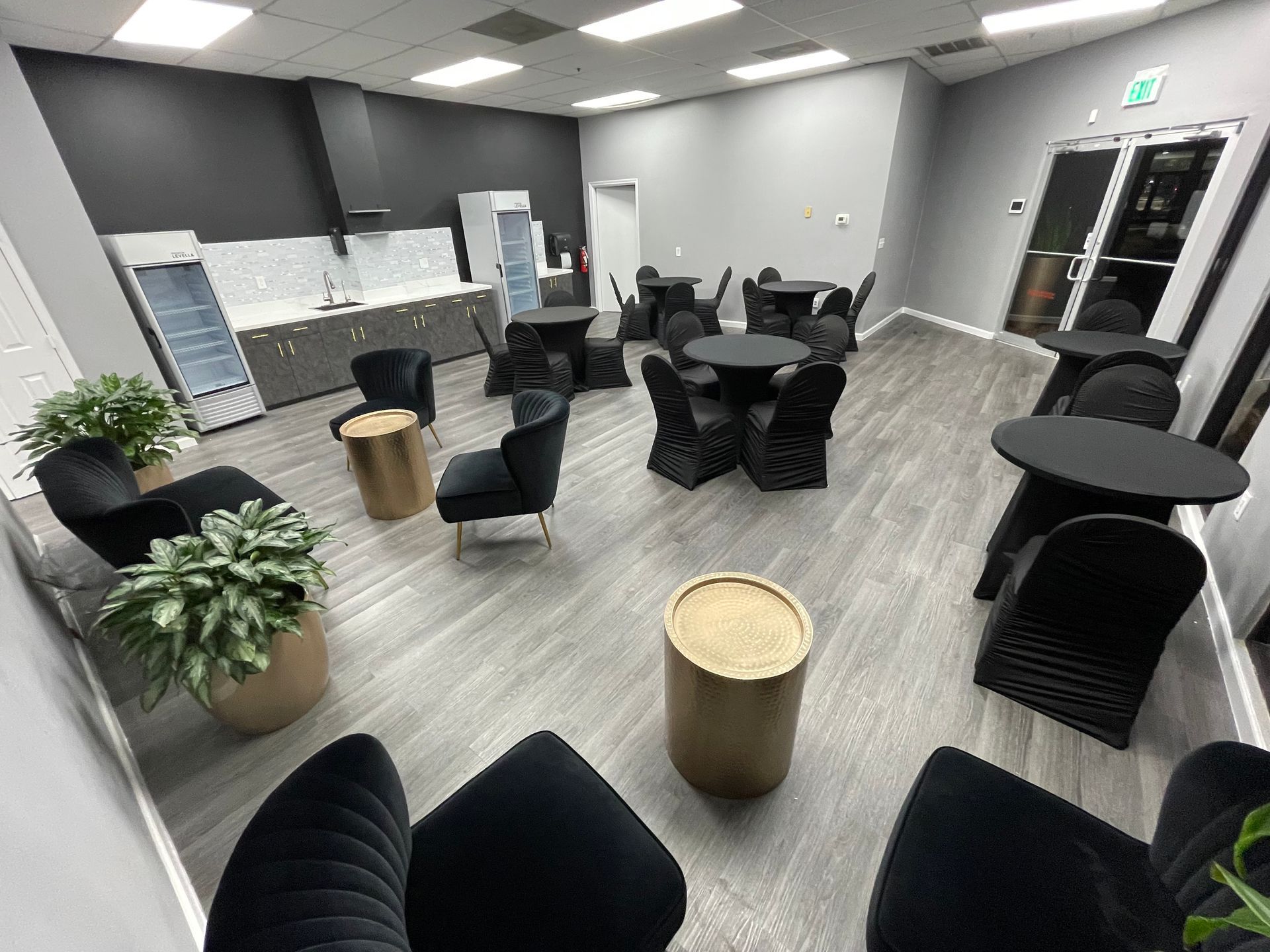 An empty room with black furniture, including chairs and tables. Light gray wood-look flooring. Neutral walls.
