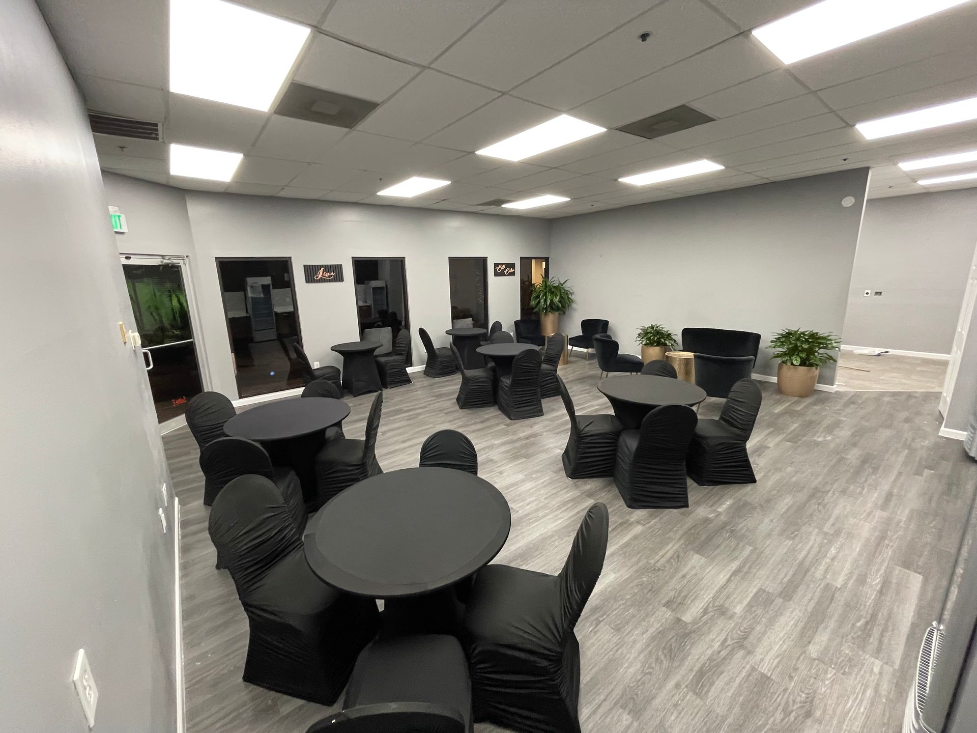 The Collective Lounge space with gray walls, round black tables and chairs, and wood-look flooring.