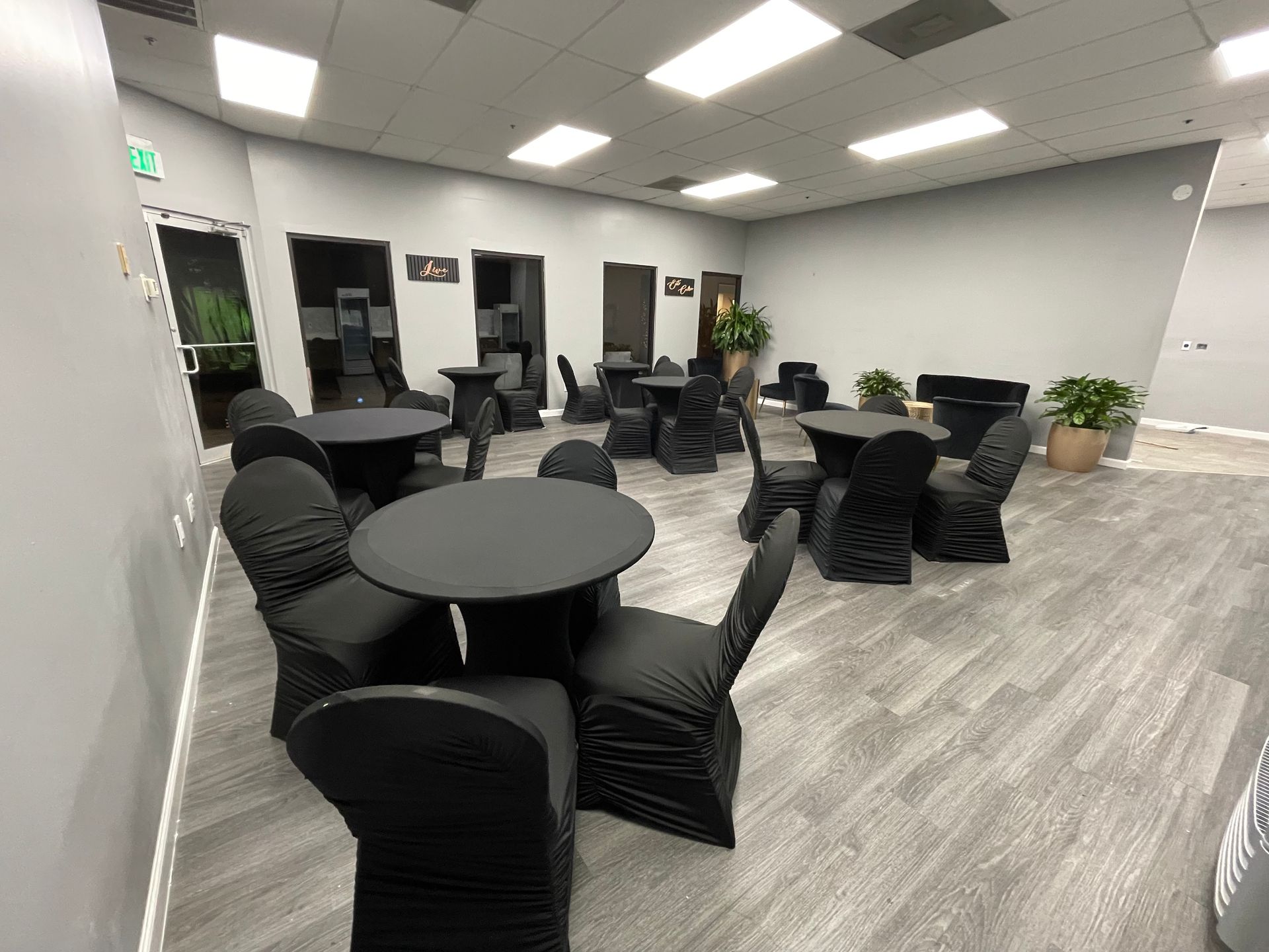 The Collective Lounge with round tables and chairs covered in black fabric. Gray walls, wood-look floor, overhead lights.