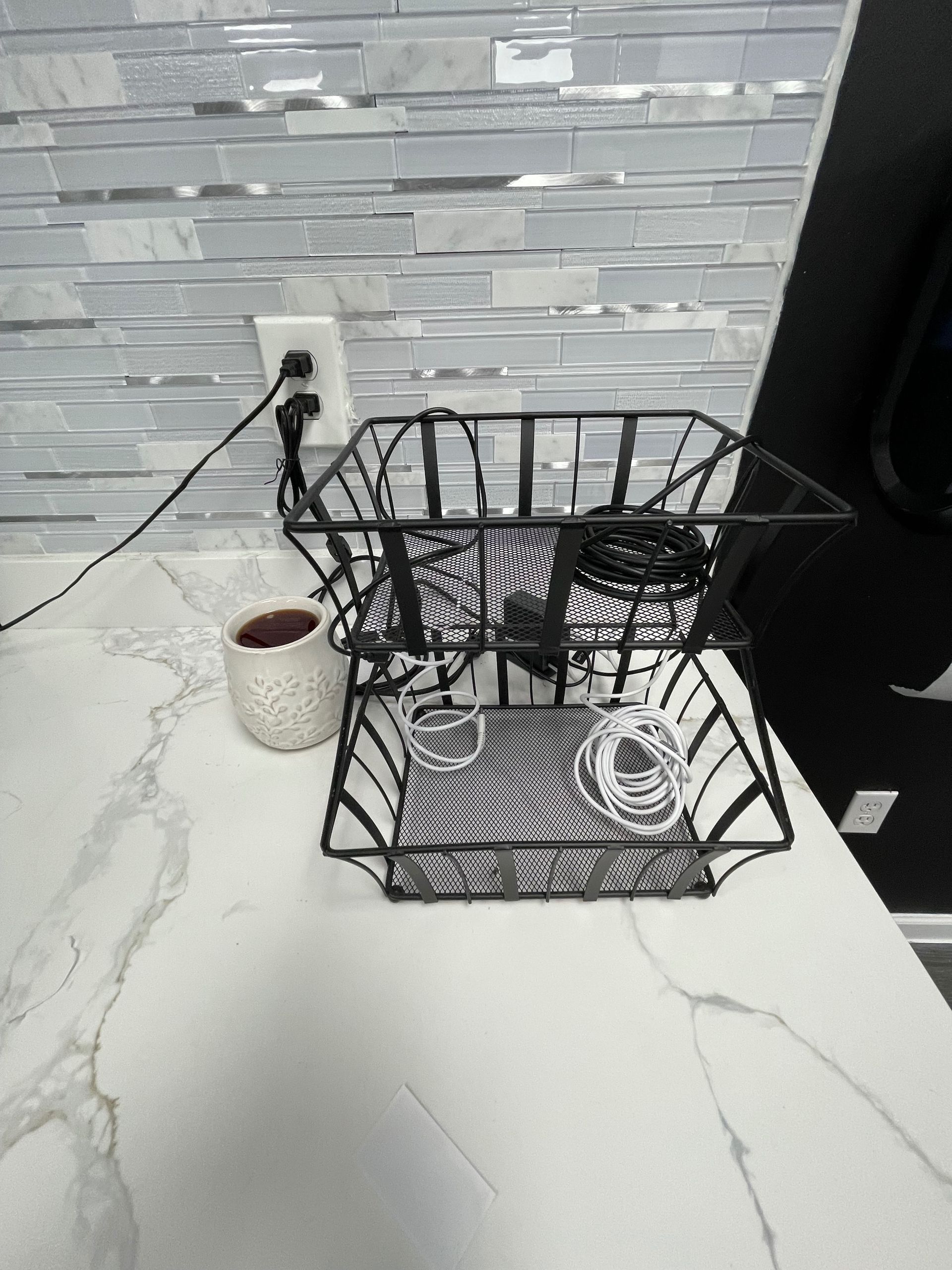 Black wire basket on a white countertop with a patterned backsplash and a small container.