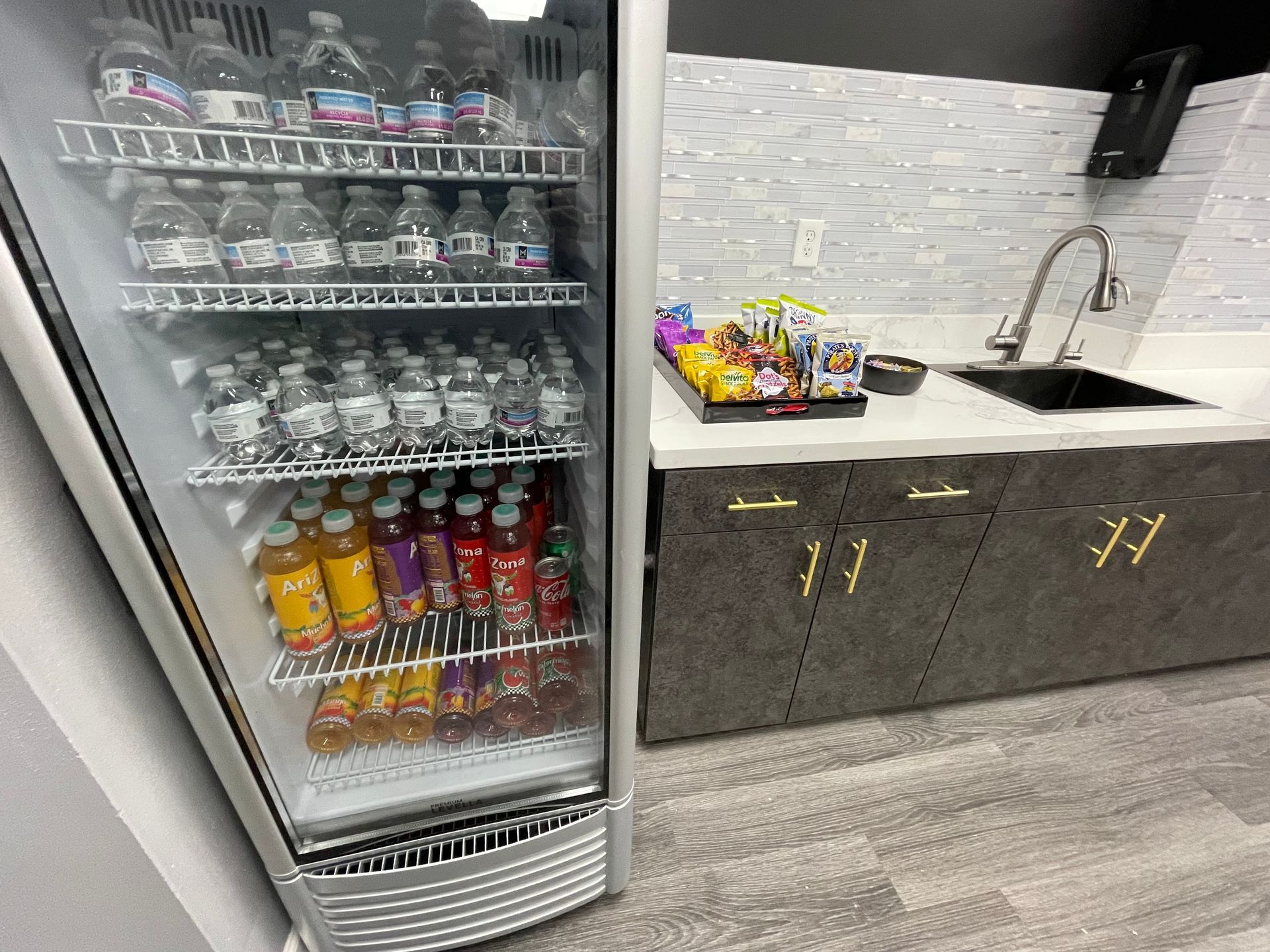 Refrigerator with drinks, snacks on countertop next to sink, and dark cabinets.