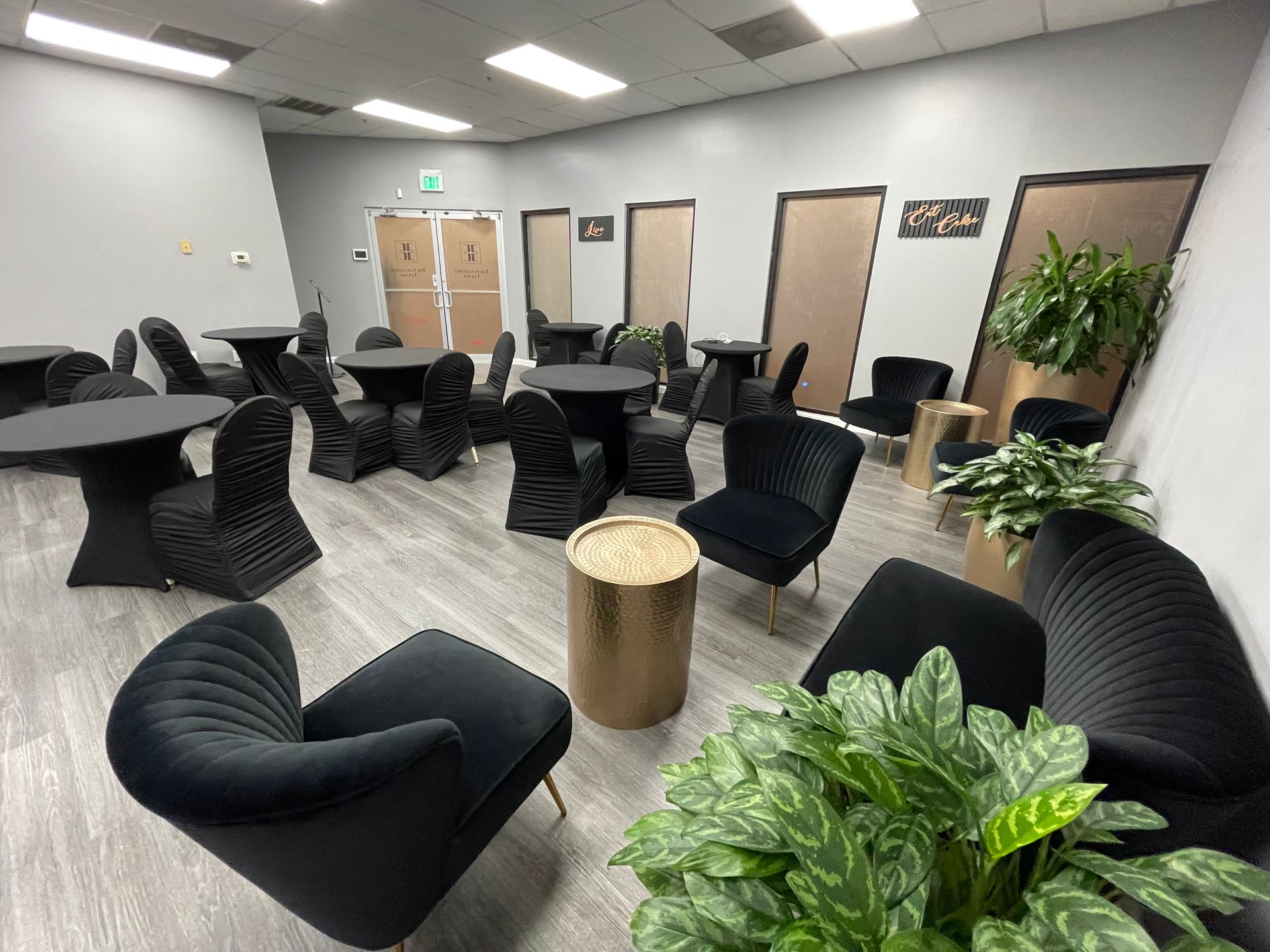 Interior room with black tables and chairs, gold accents, and plants.