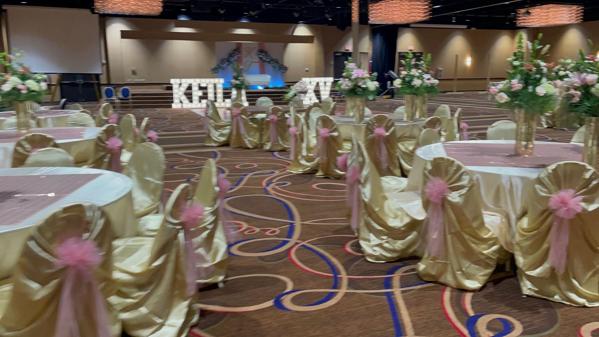 A large room with tables and chairs decorated for a quinceañera.