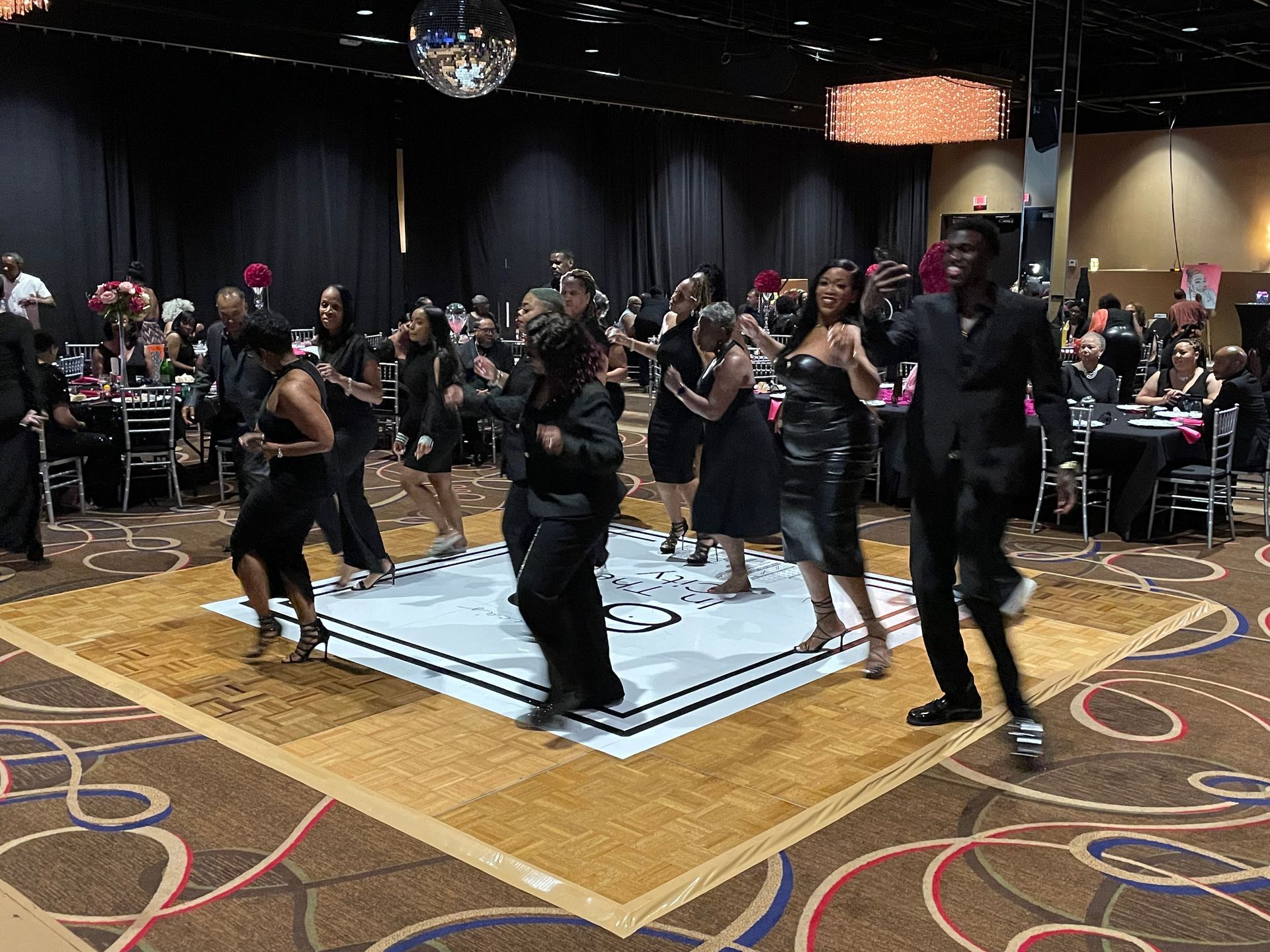 A group of people are dancing on a dance floor in a large room.