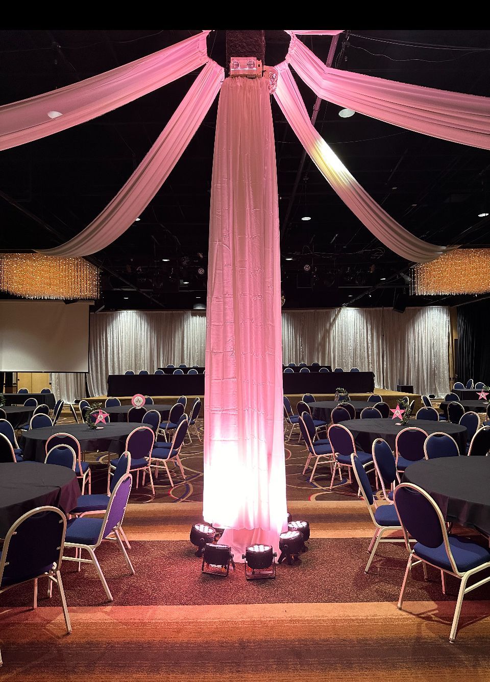 A large room with tables and chairs and a pink curtain hanging from the ceiling.