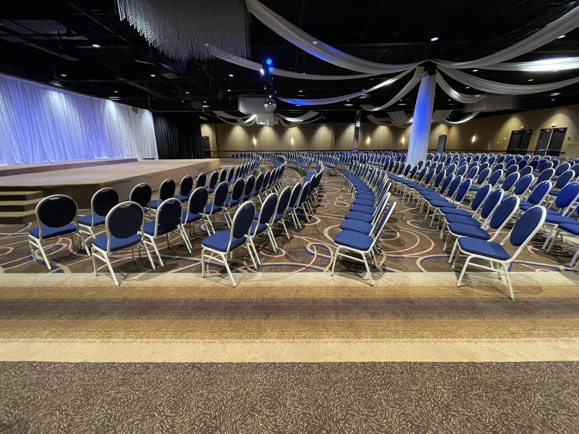 A large auditorium filled with rows of blue chairs and a stage.