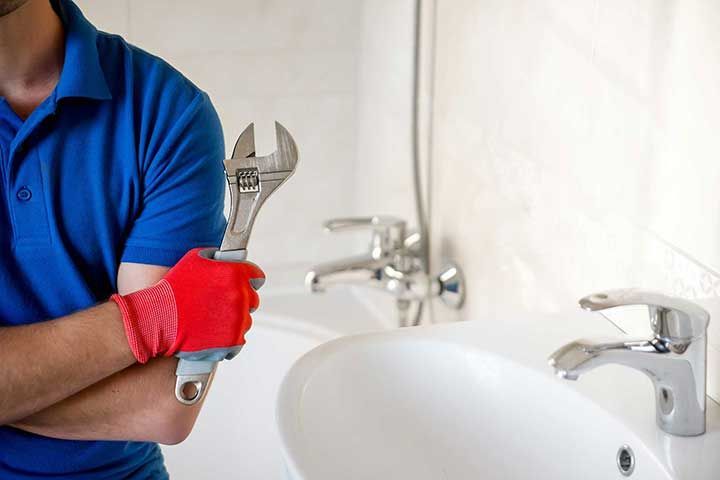 plumber with wrench standing in bathroom 

